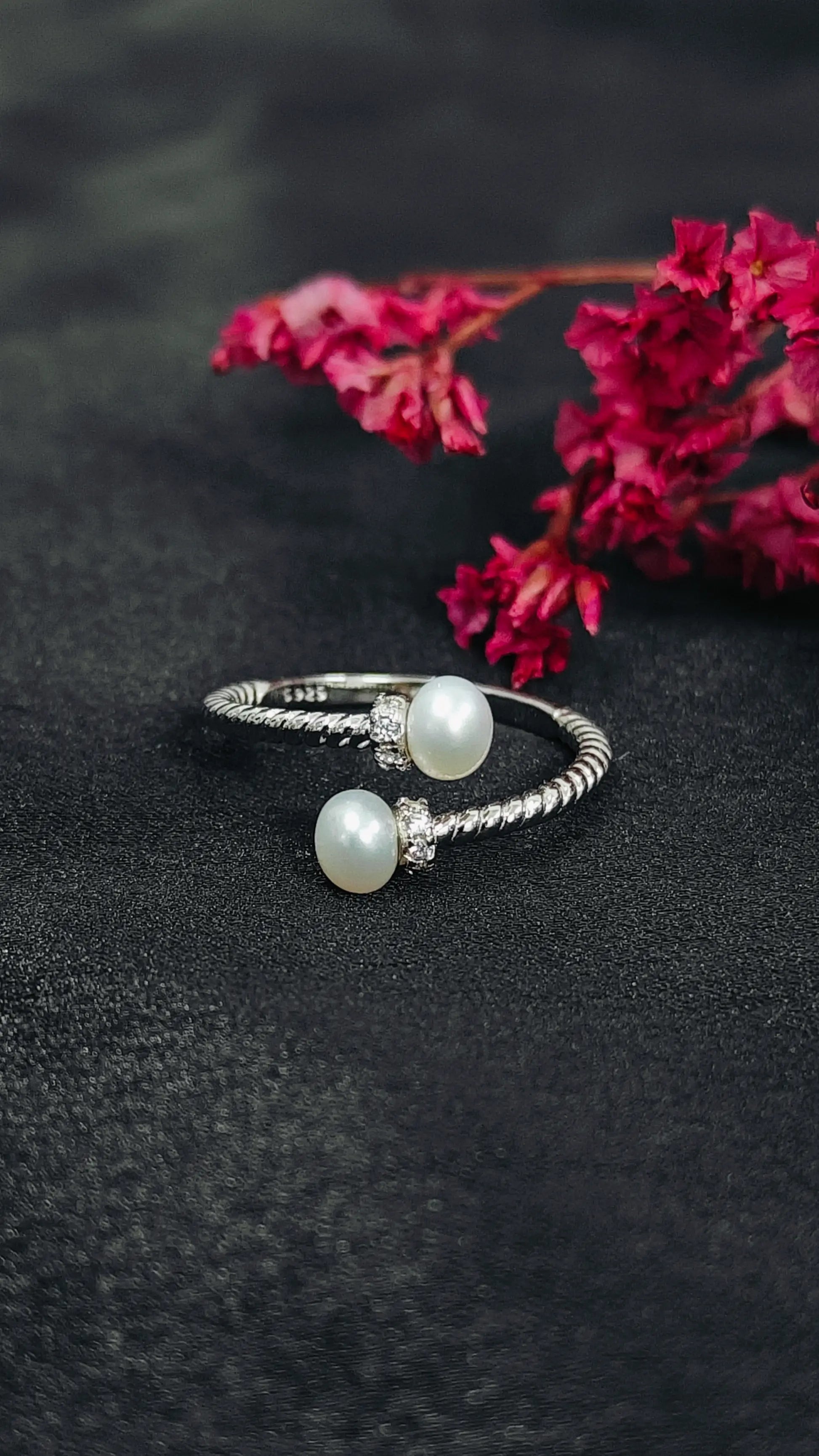 Silver ring with pearl beads on a dark surface with pink flowers in the background