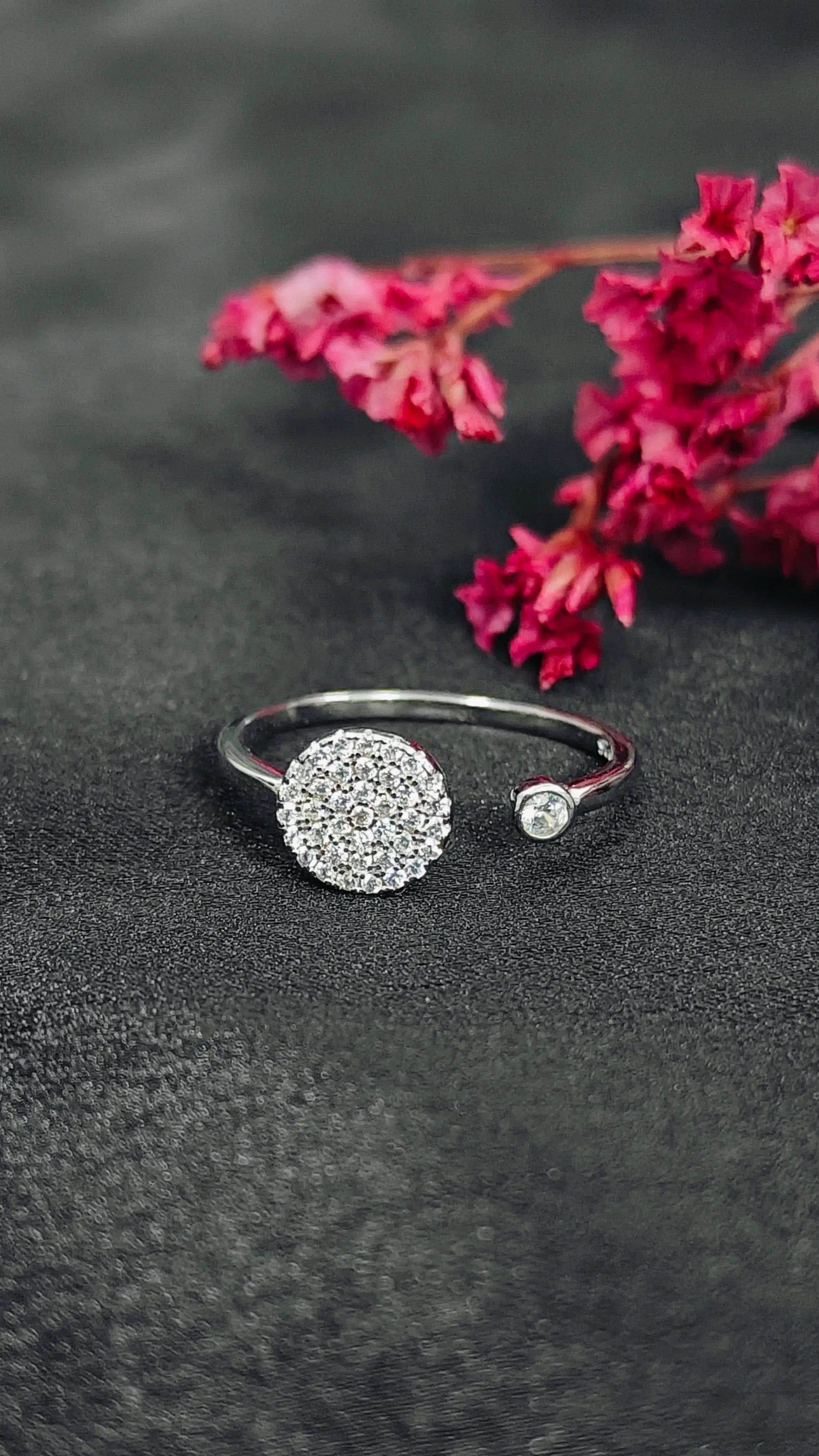 Silver ring with a textured ball design on a dark surface with pink flowers.