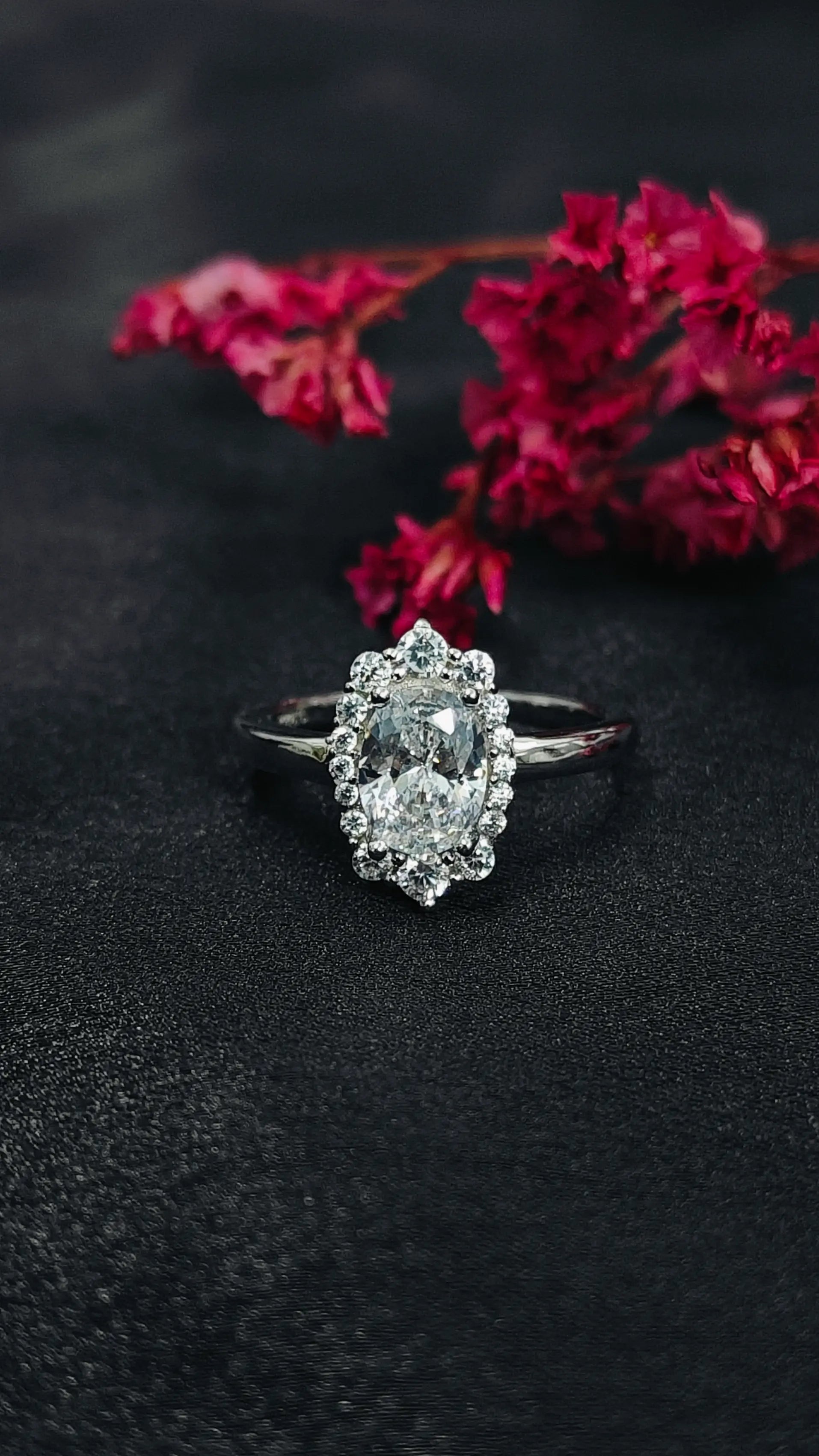 Diamond ring on a dark surface with red flowers in the background