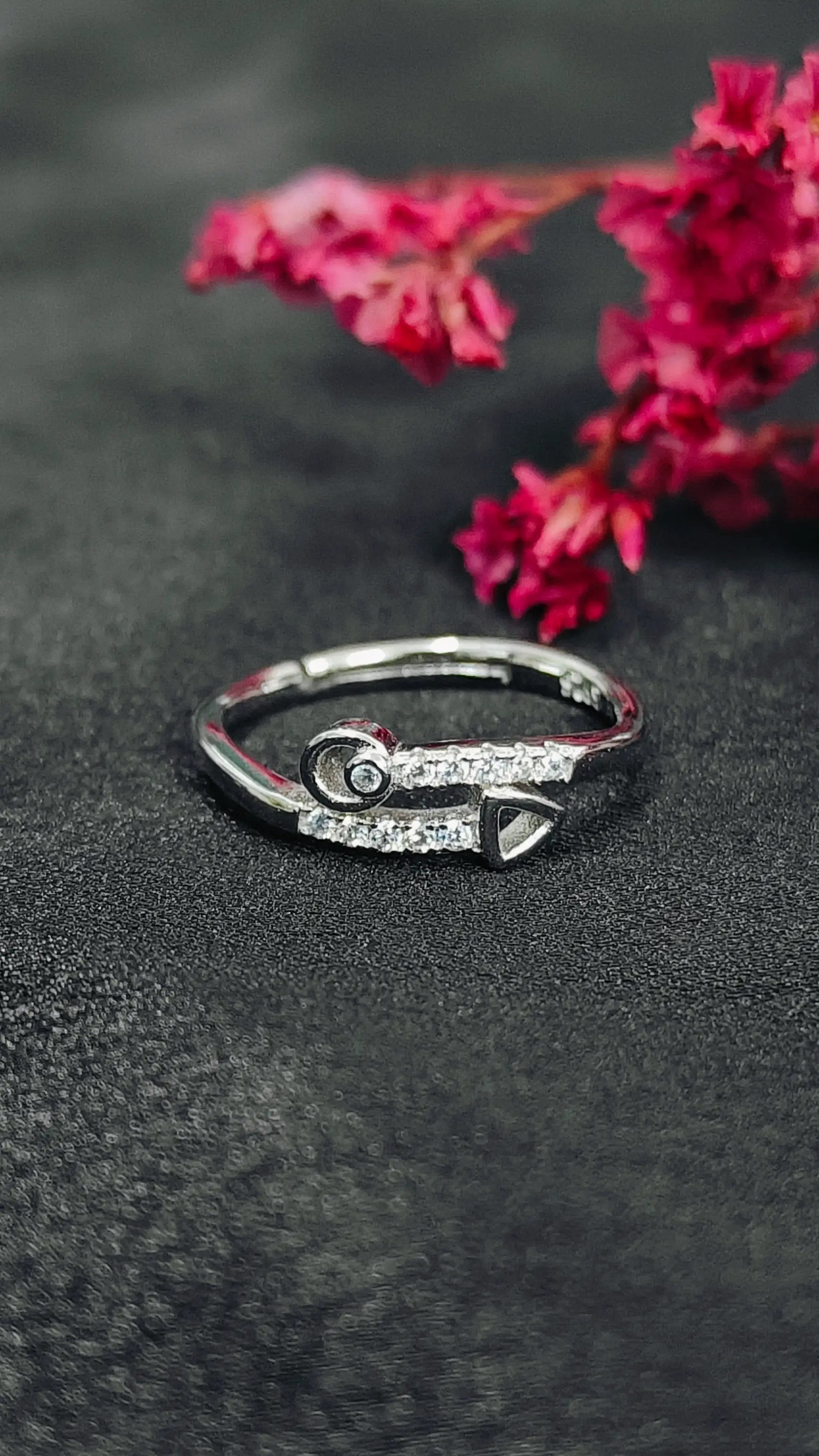 Silver ring with gemstones on a dark surface with pink flowers in the background
