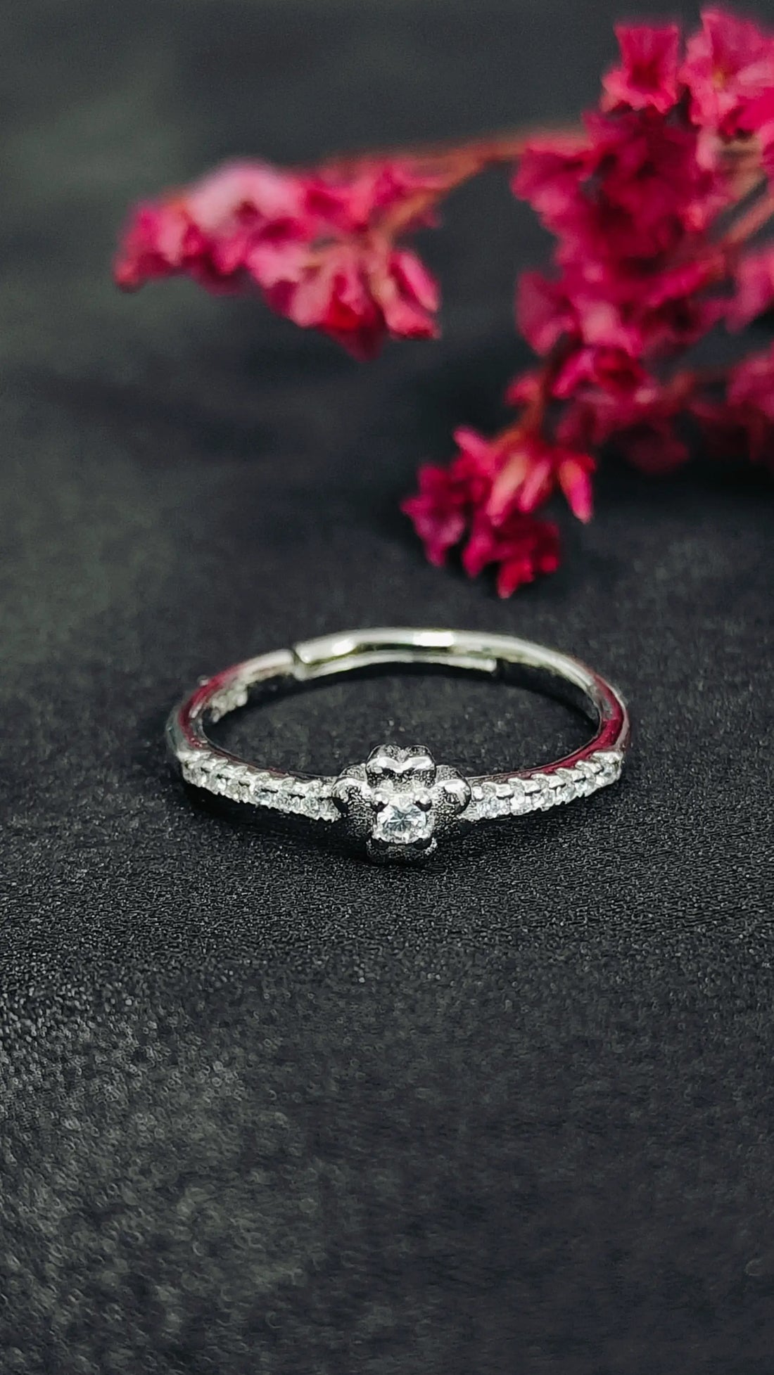 Silver ring with a diamond on a dark surface with pink flowers in the background