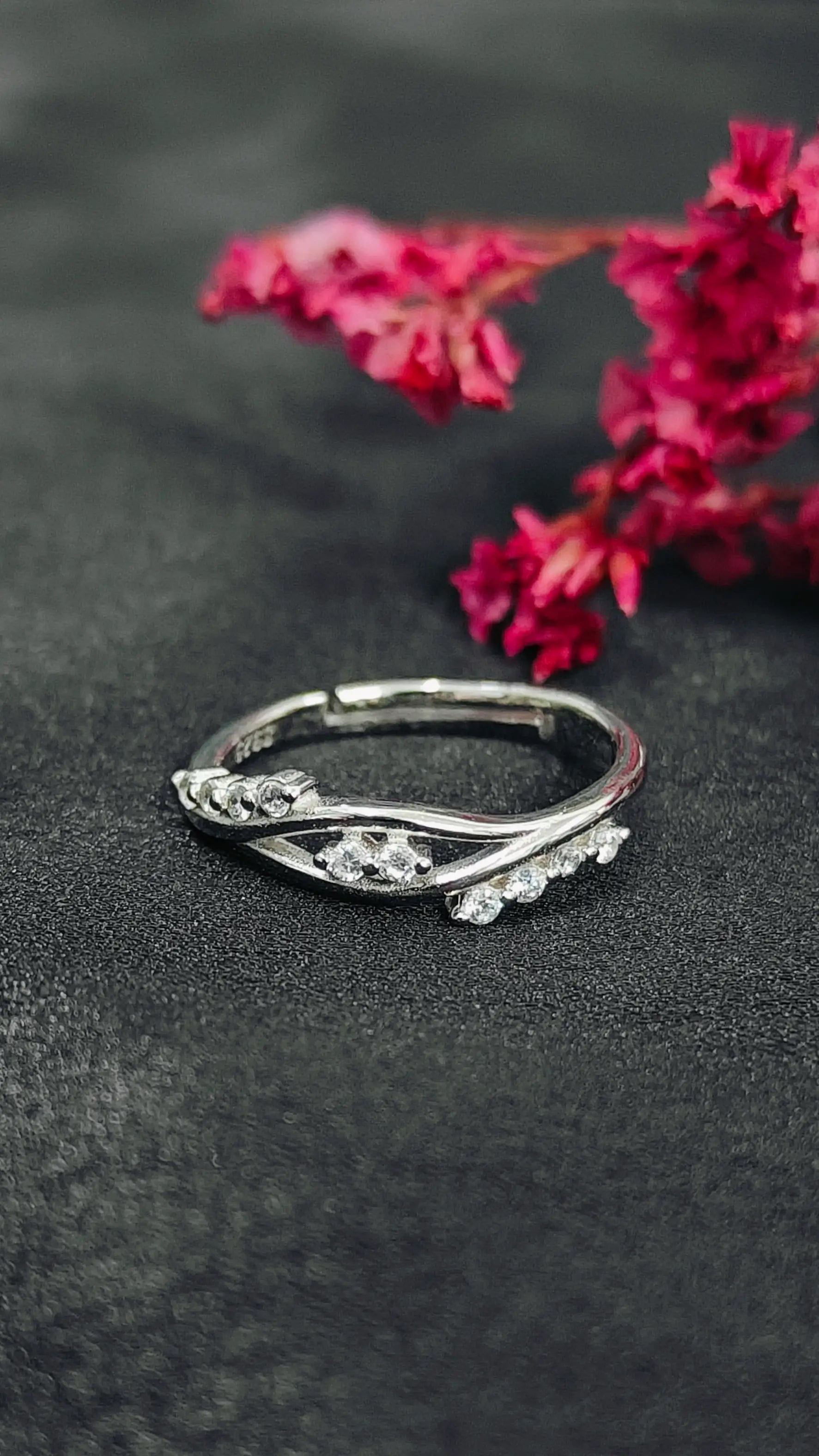 Silver ring with floral design on a dark surface with pink flowers in the background