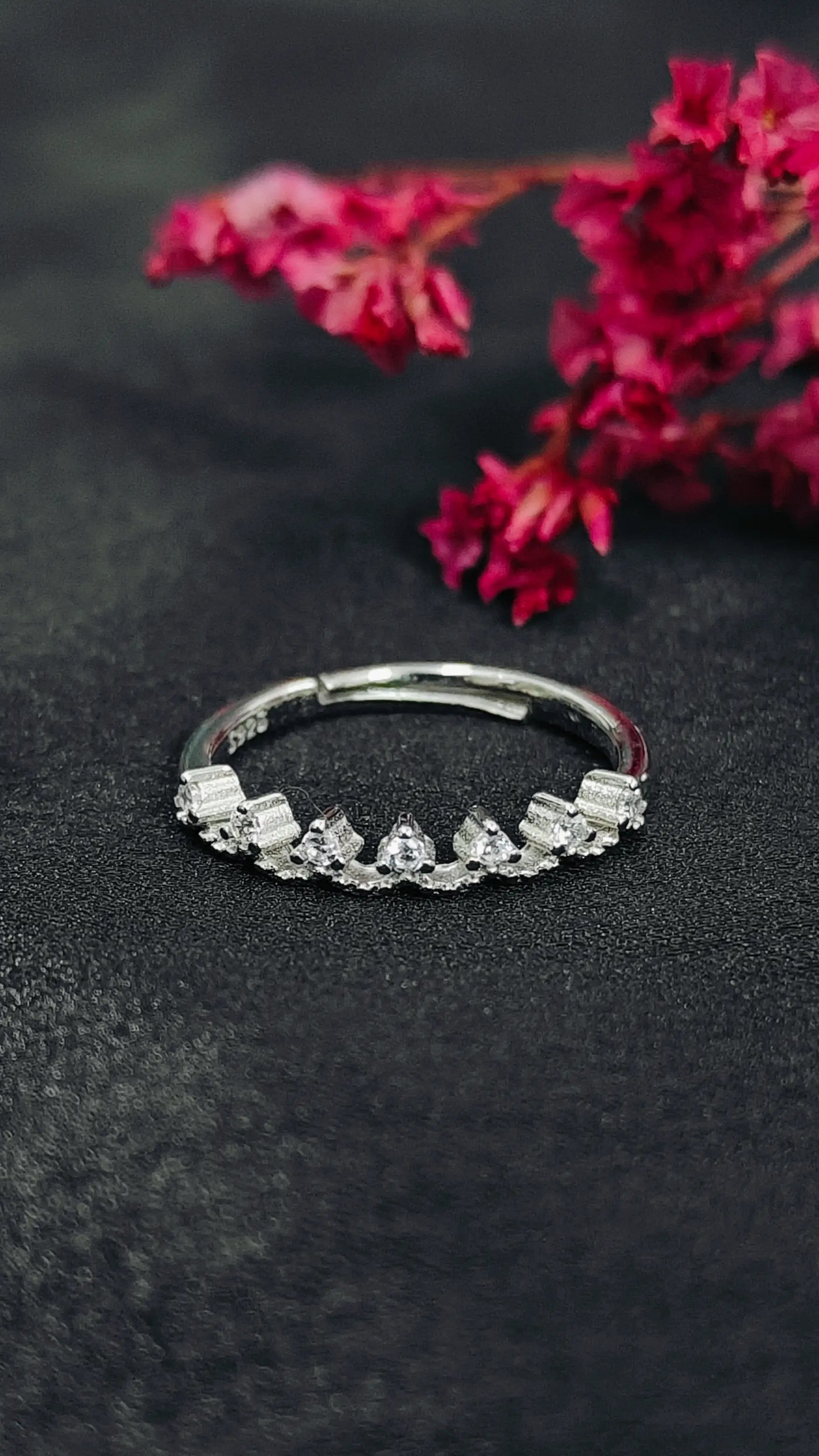 Silver ring with small diamonds on a dark surface with pink flowers in the background