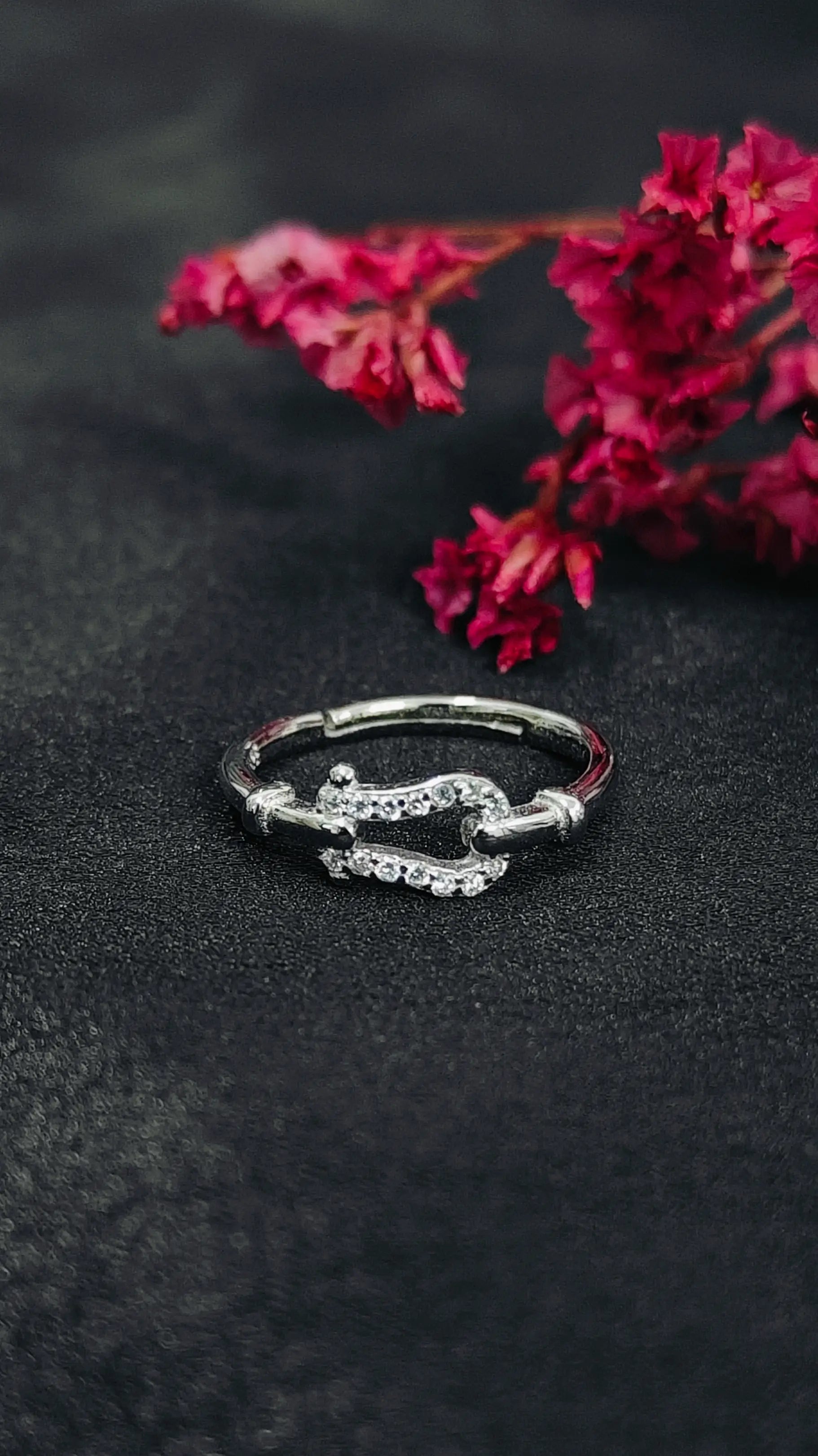 Silver ring with red gemstones on a dark surface with pink flowers