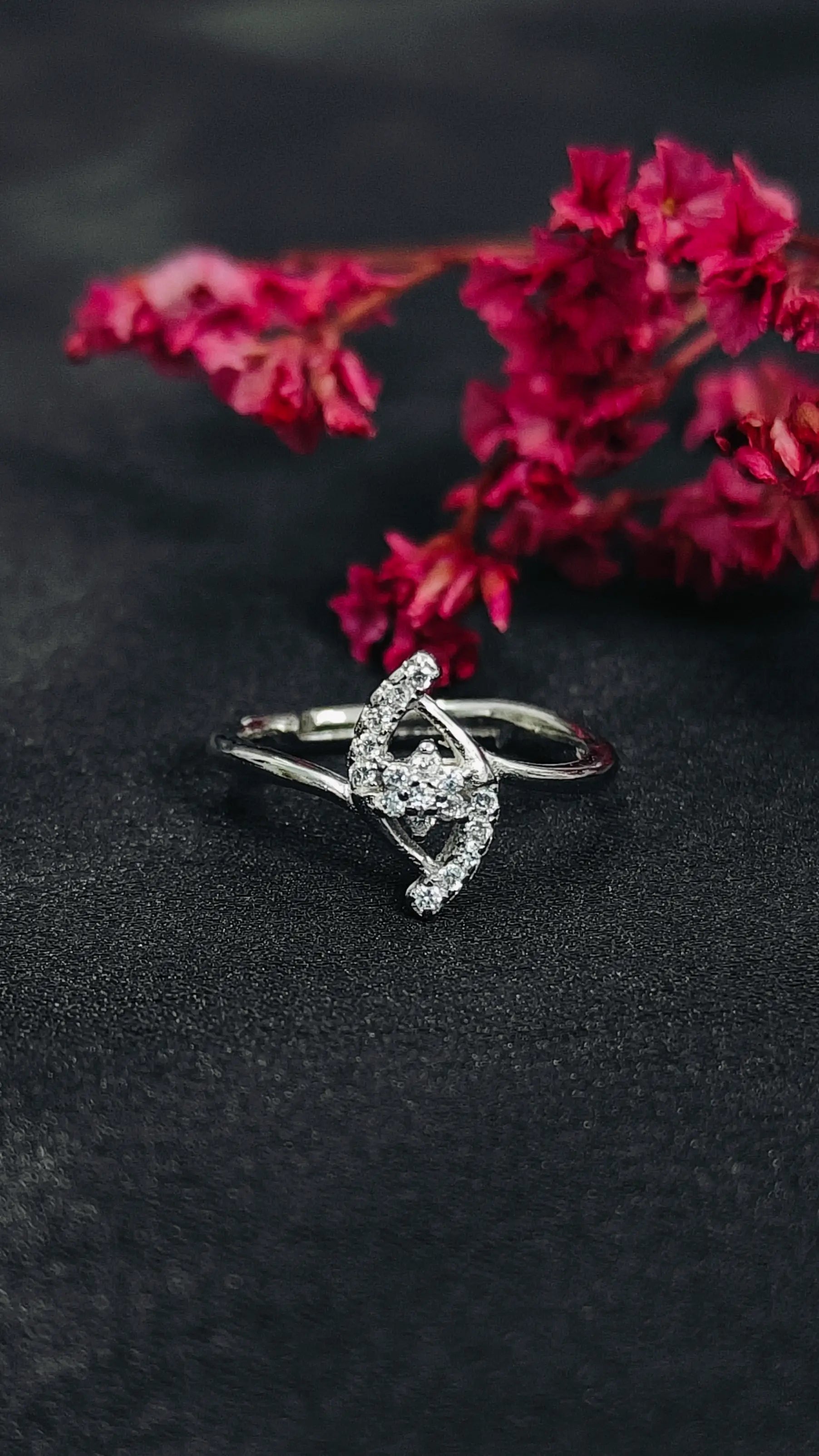 Silver ring with a decorative design on a dark surface with pink flowers in the background