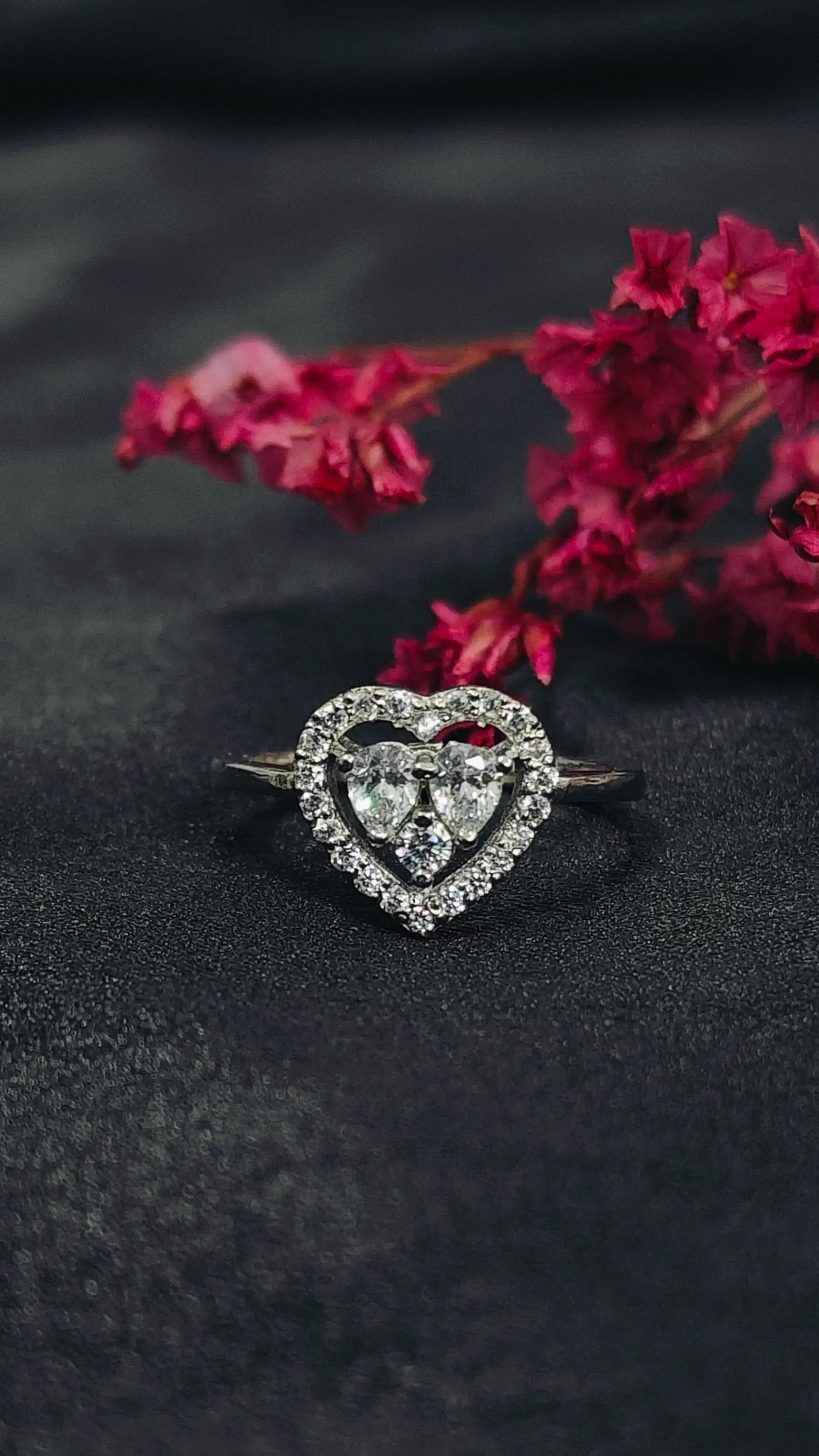 Heart-shaped diamond ring on a dark surface with pink flowers