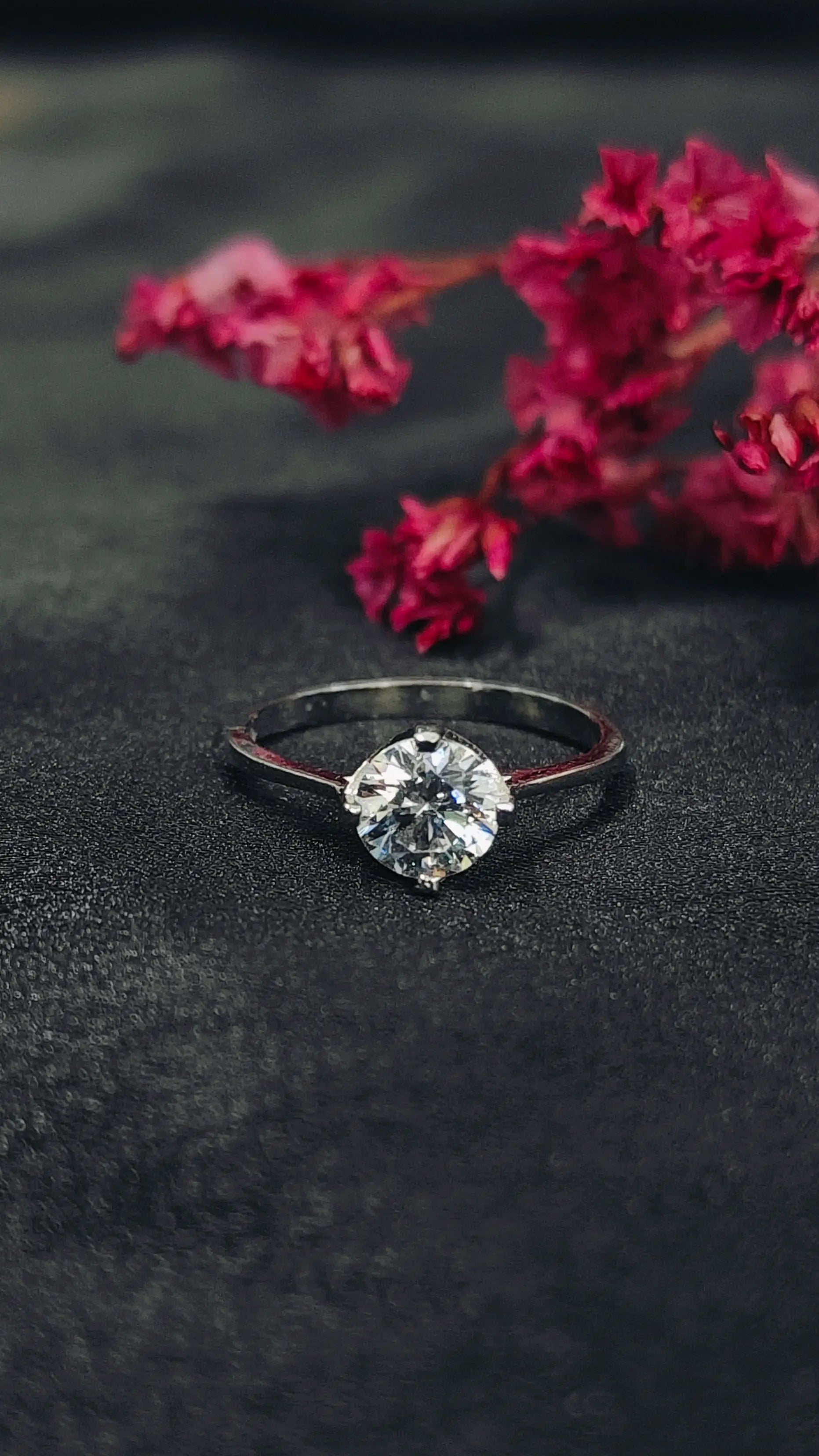 Diamond ring on a dark surface with pink flowers in the background