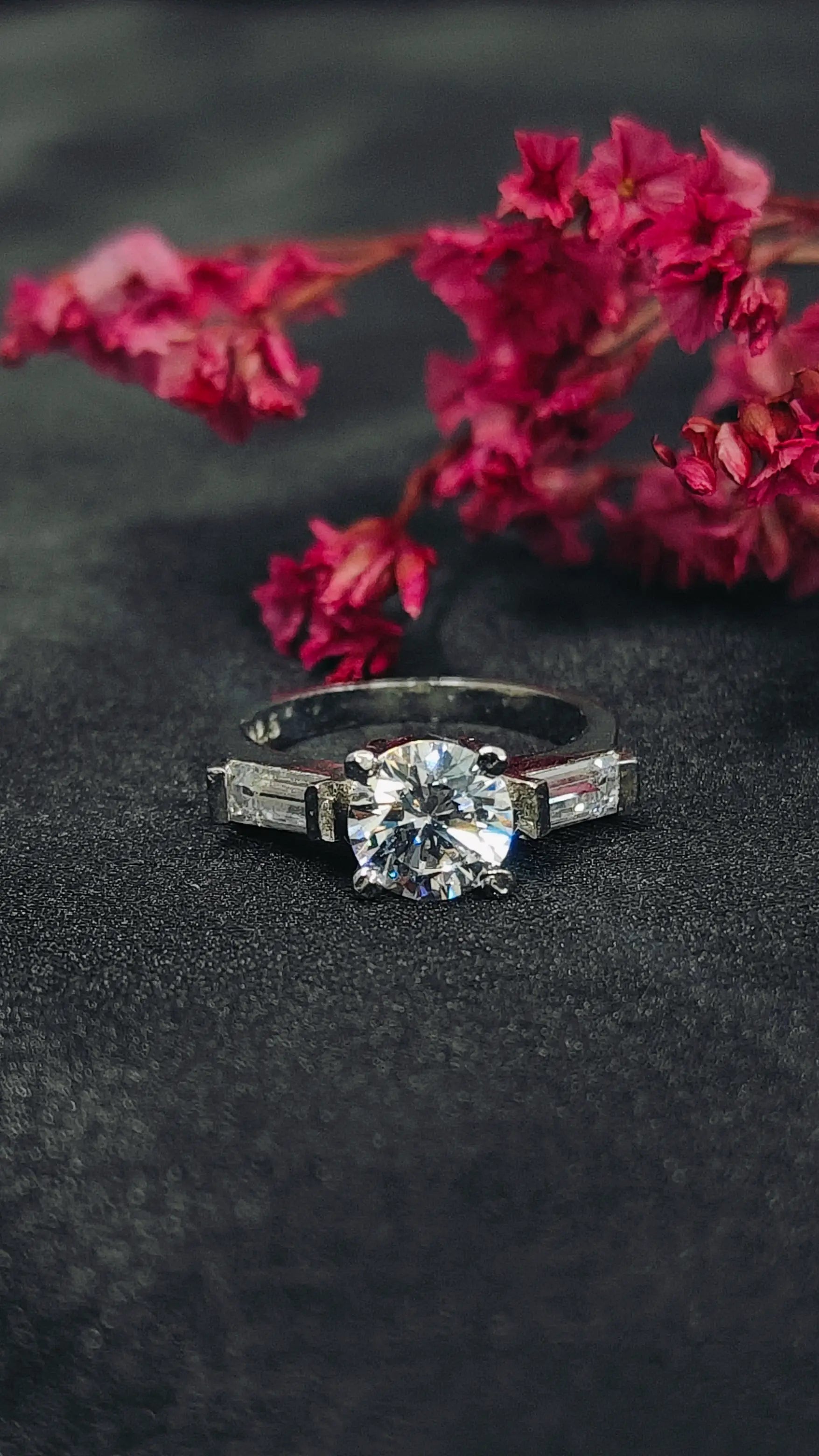 Diamond ring on a dark surface with pink flowers in the background