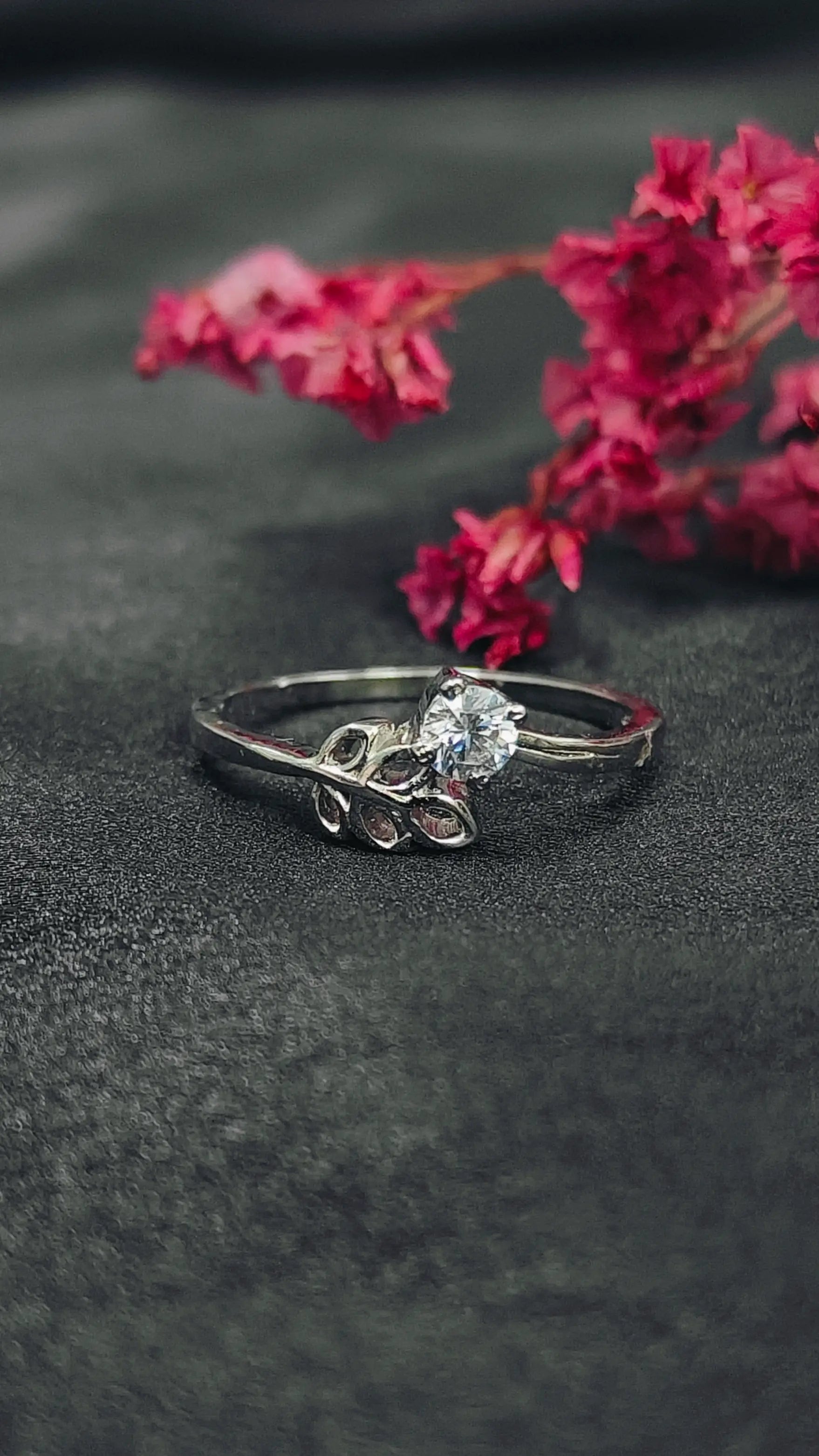 Silver ring with a diamond on a dark surface with pink flowers