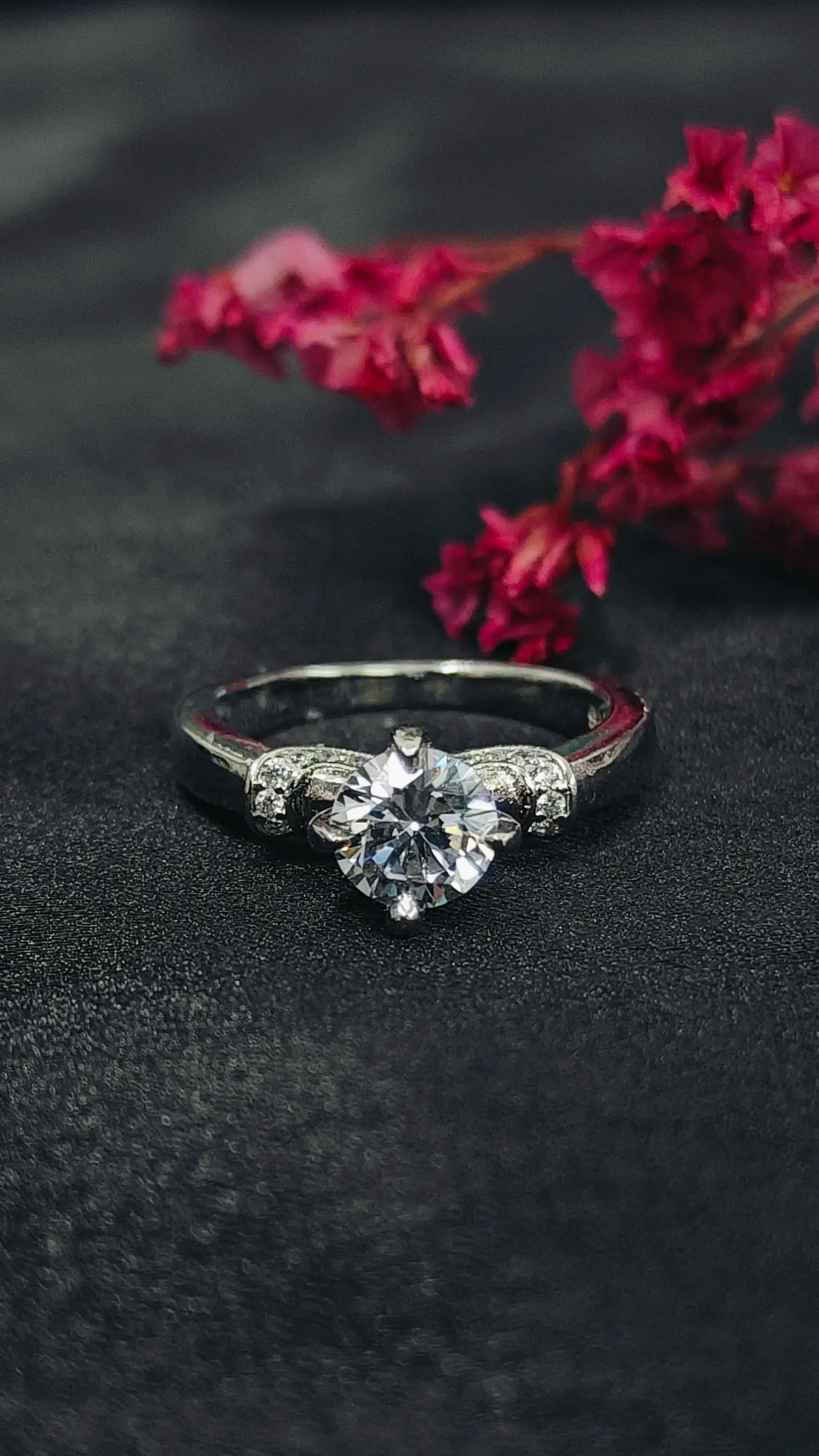 Diamond ring on a dark surface with red flowers in the background