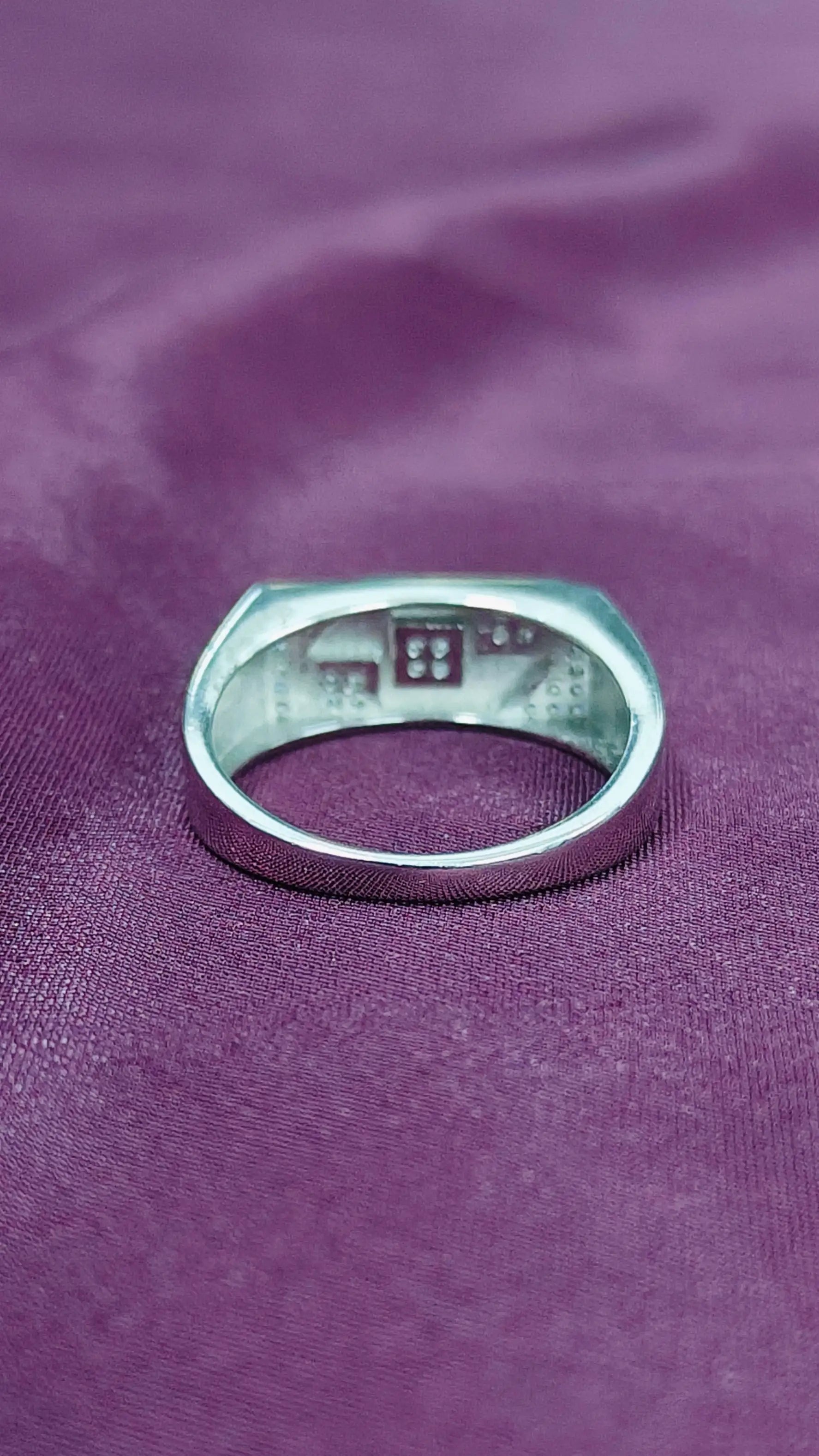 Silver ring with engraved text on a purple fabric background