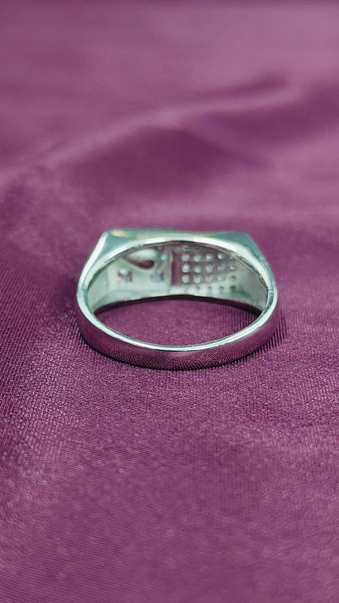 Silver ring with engraved text on a purple fabric background
