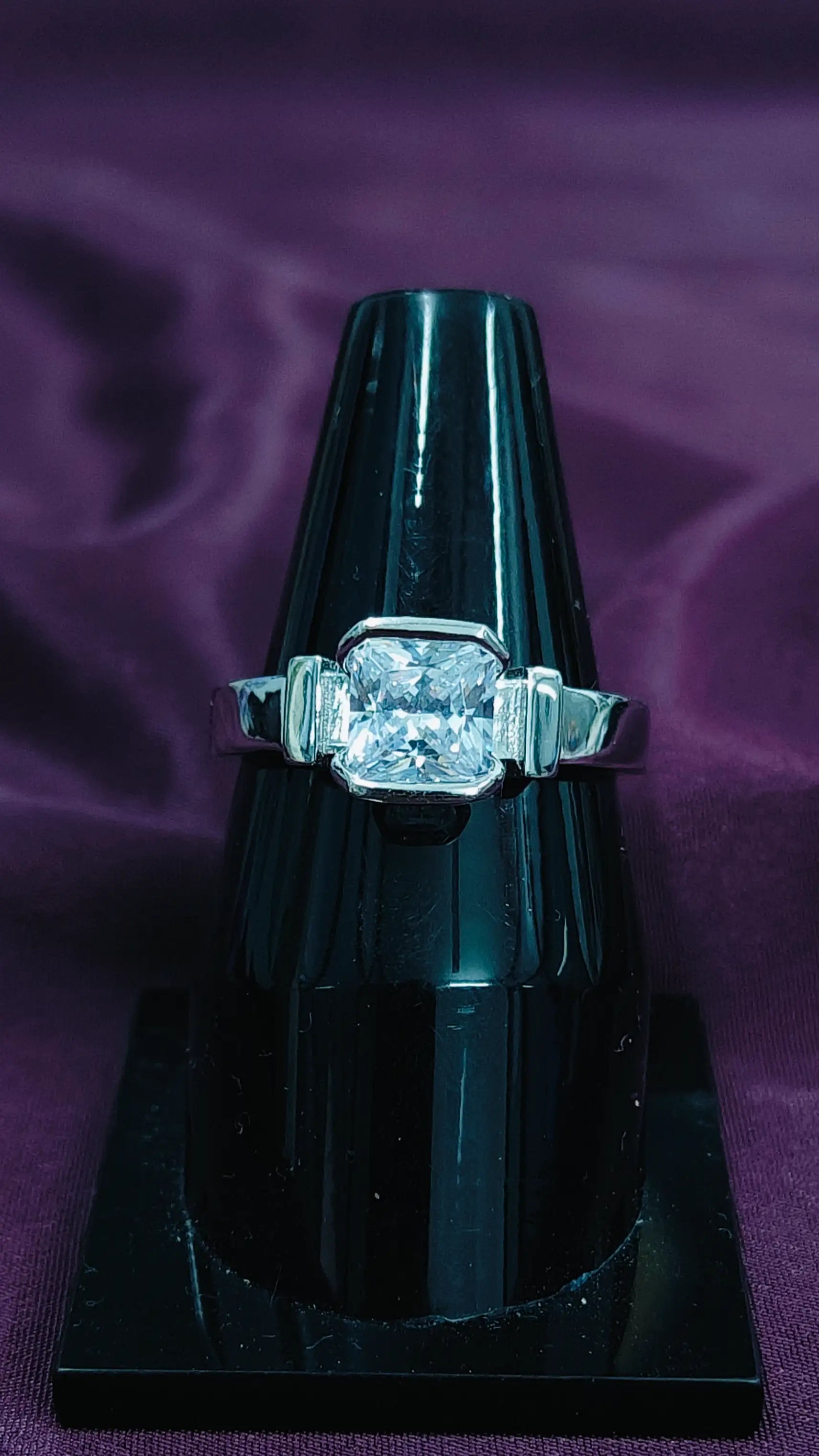 Diamond ring on a black stand against a purple background