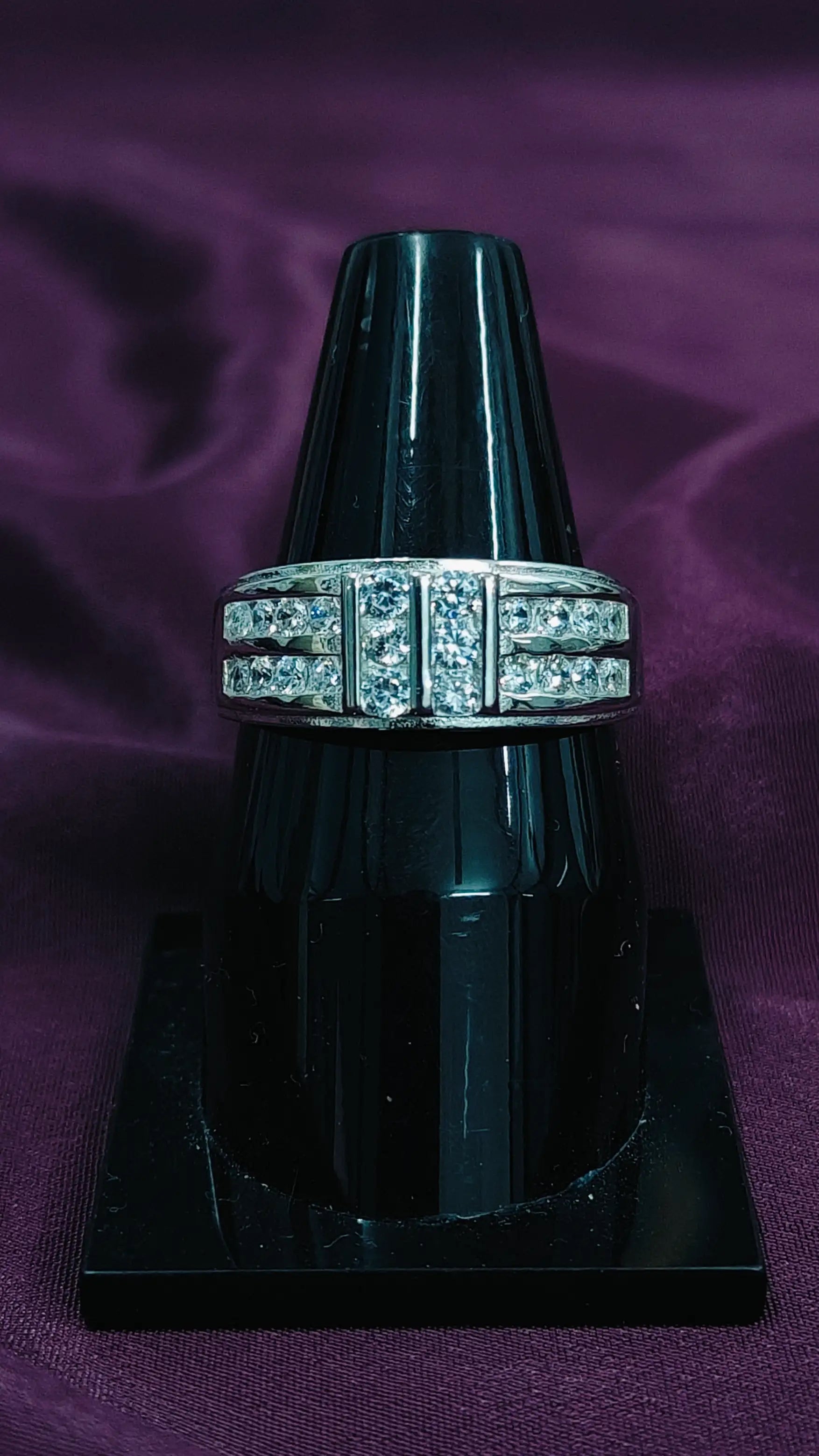 Ring with diamond accents on a black stand against a purple fabric background