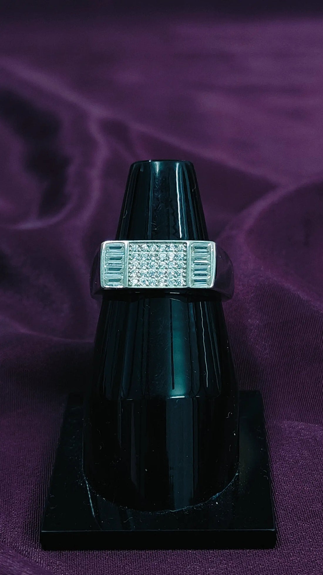 Black ring with a diamond-like center on a purple fabric background