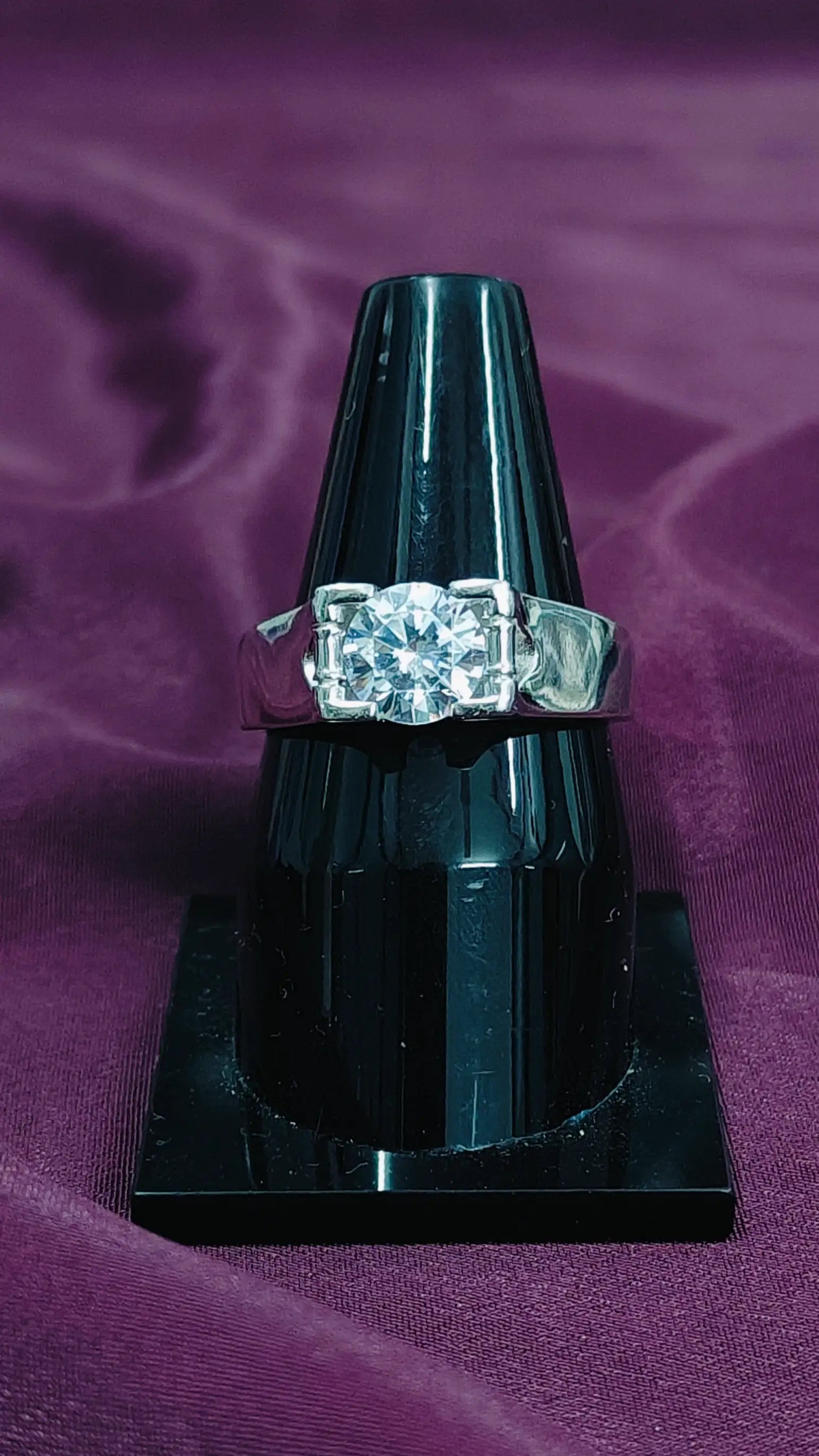 Diamond ring on a black stand against a purple fabric background