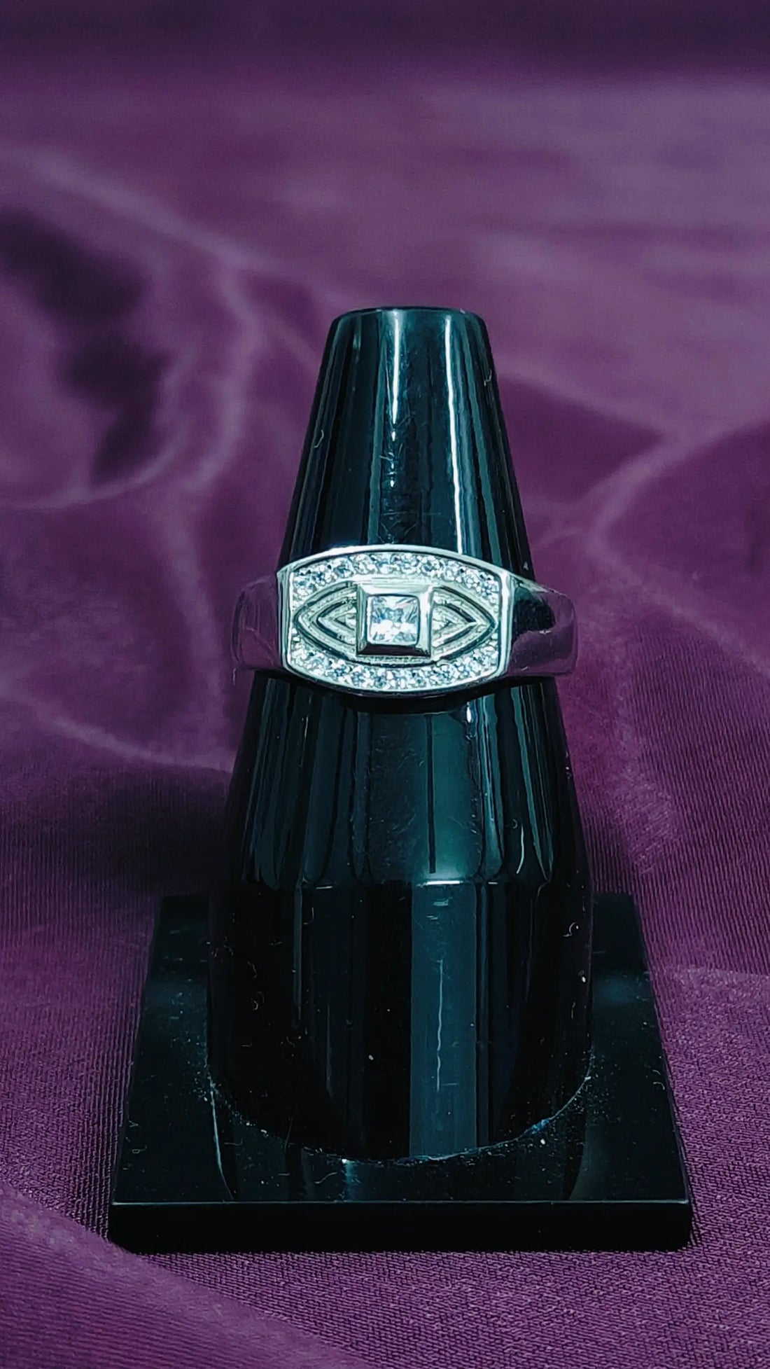 Silver ring with a diamond on a black stand against a purple background