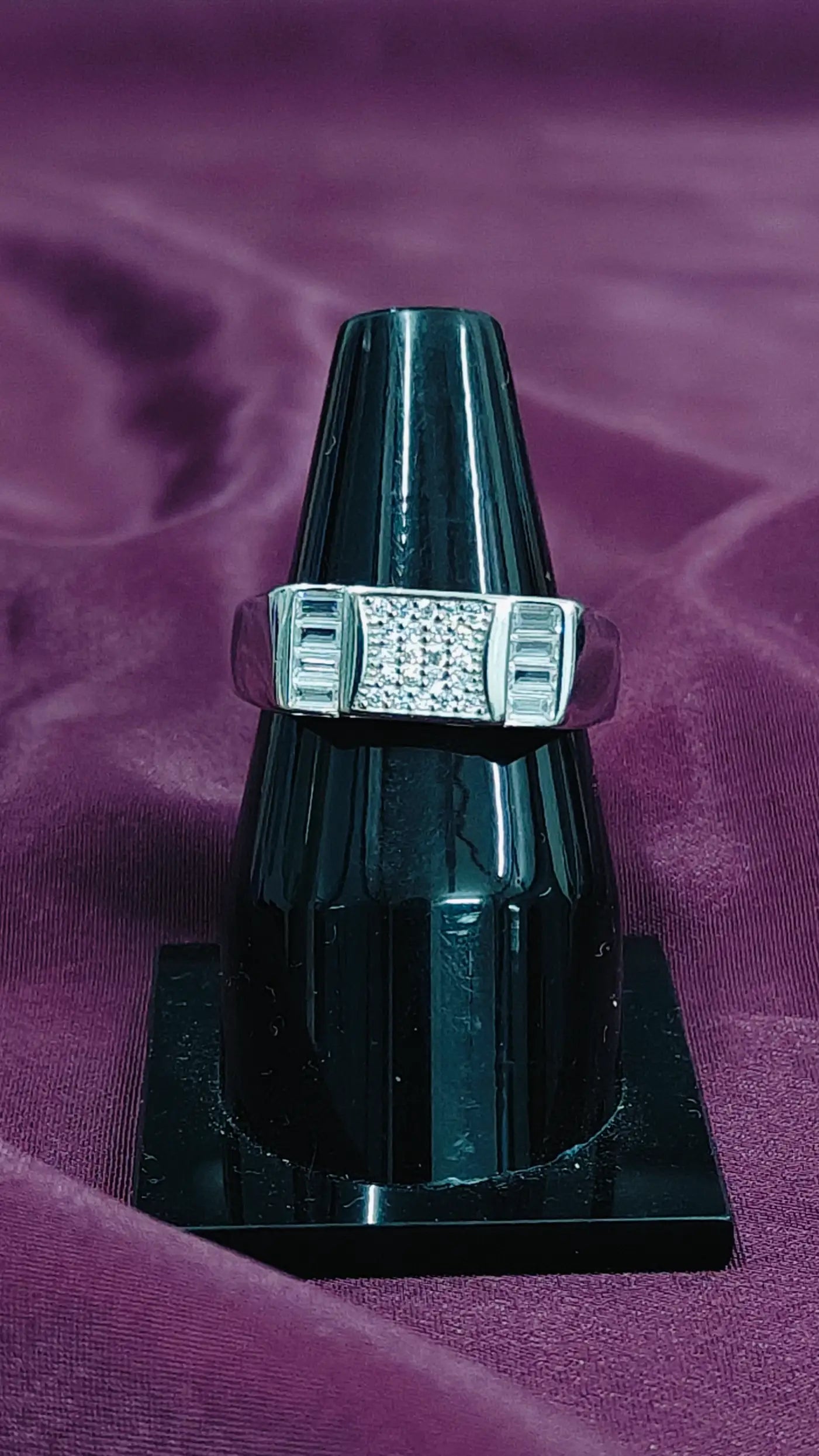 Silver ring with a black stand on a purple fabric background