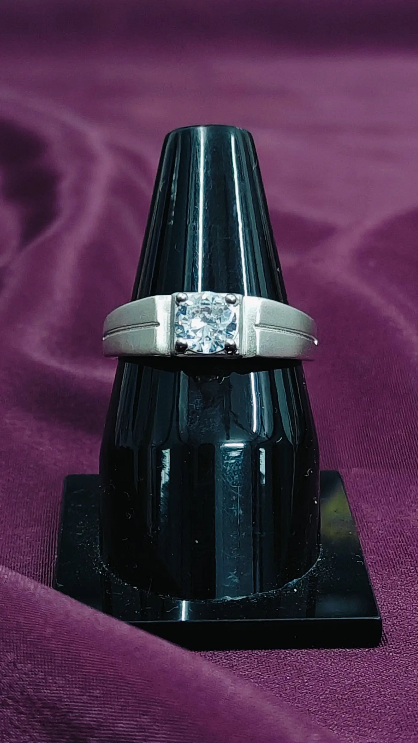 Diamond ring on a black stand against a purple fabric background