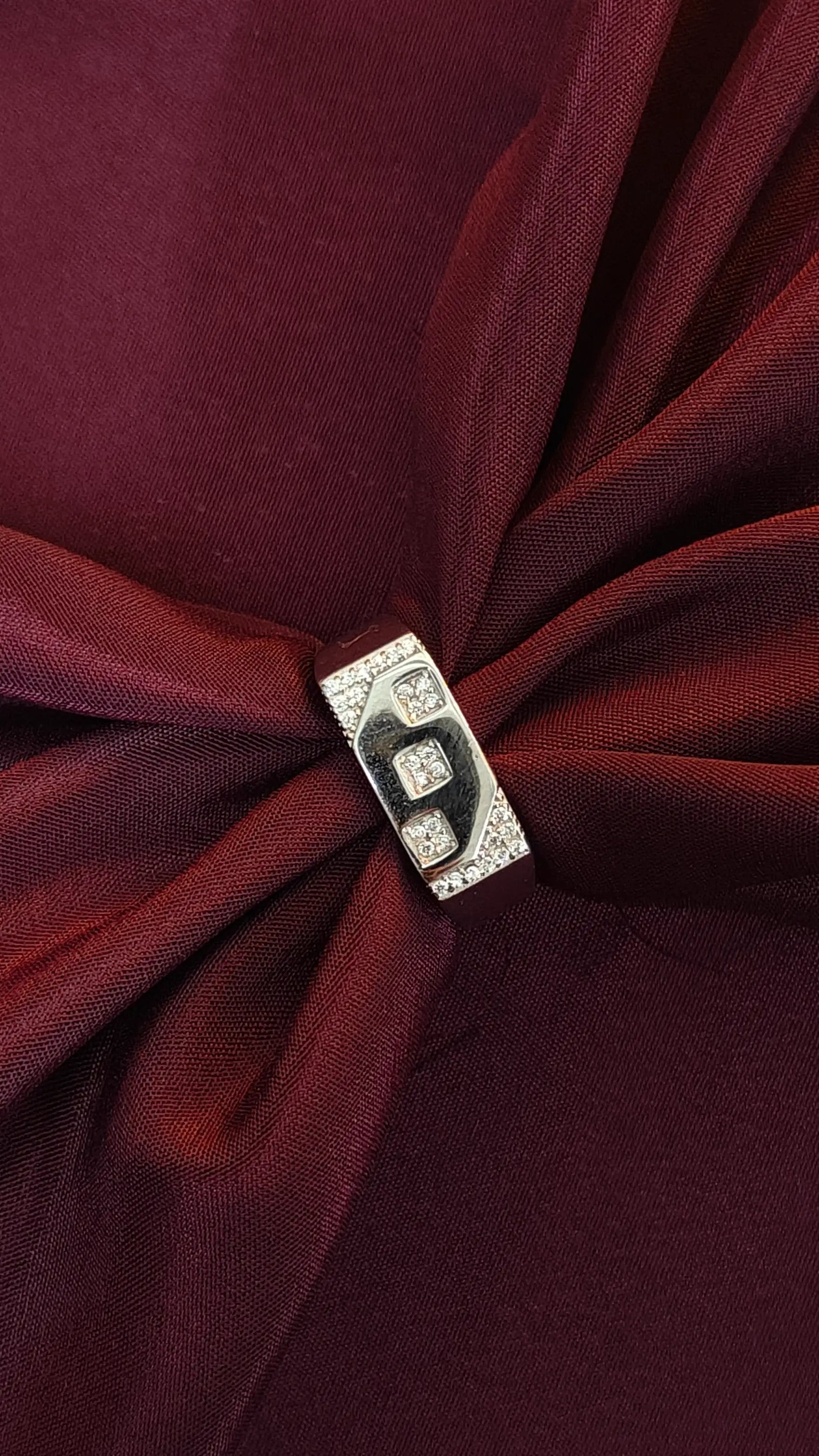 Close-up of a burgundy fabric with a decorative brooch featuring the letter 'B'.