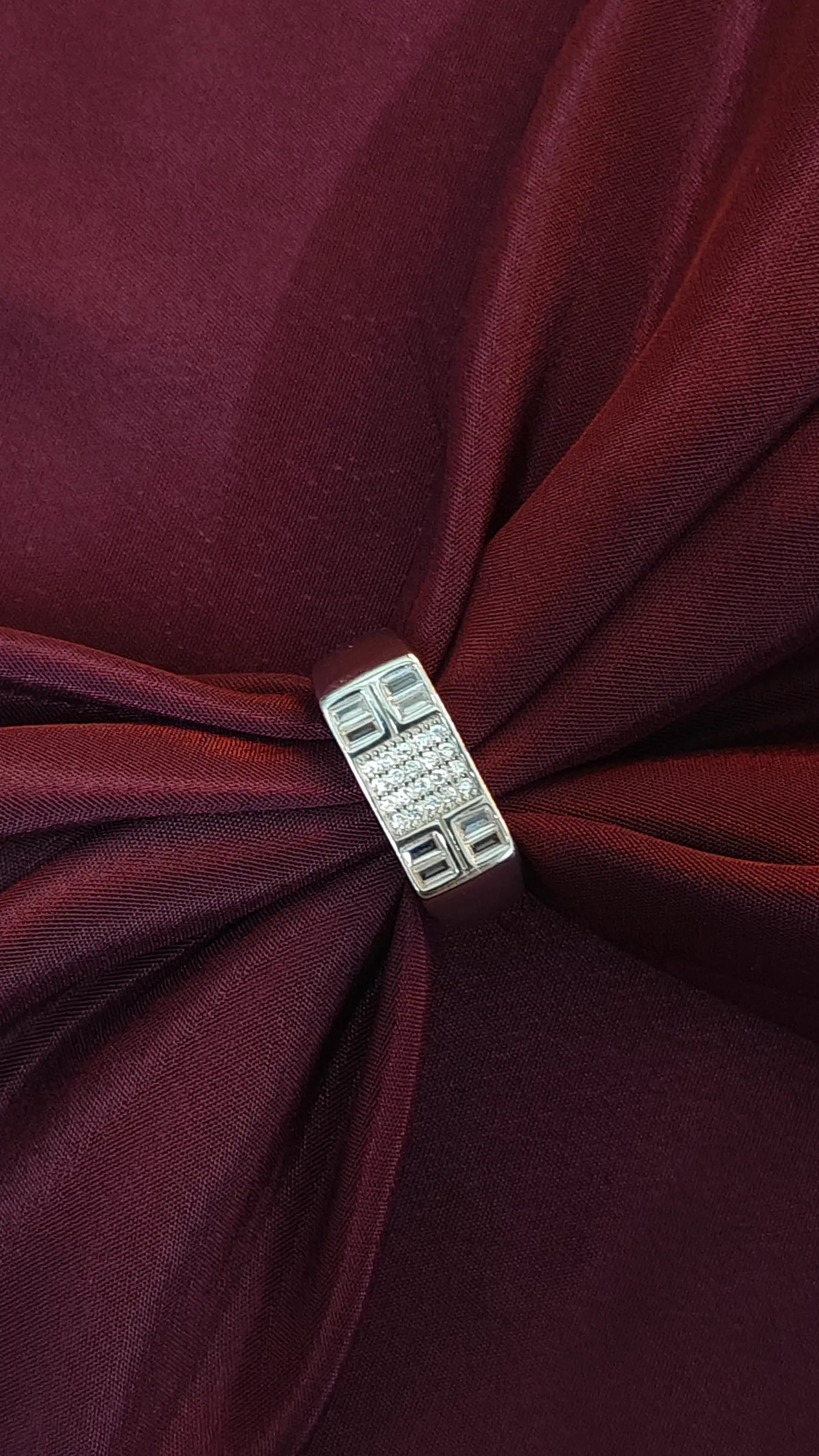 Close-up of a burgundy fabric with a decorative silver brooch.