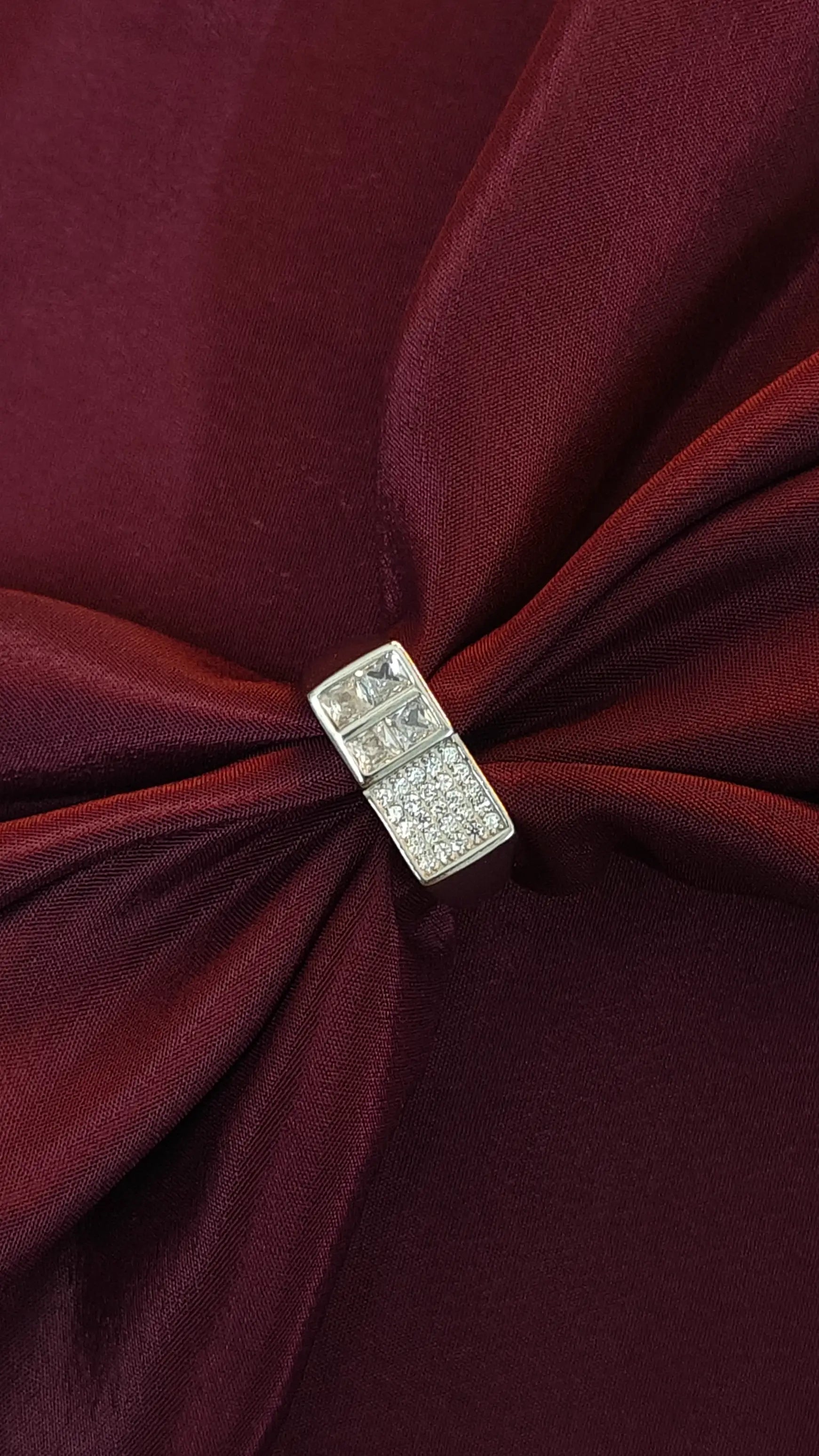 Close-up of a burgundy fabric with a decorative brooch featuring small diamonds.