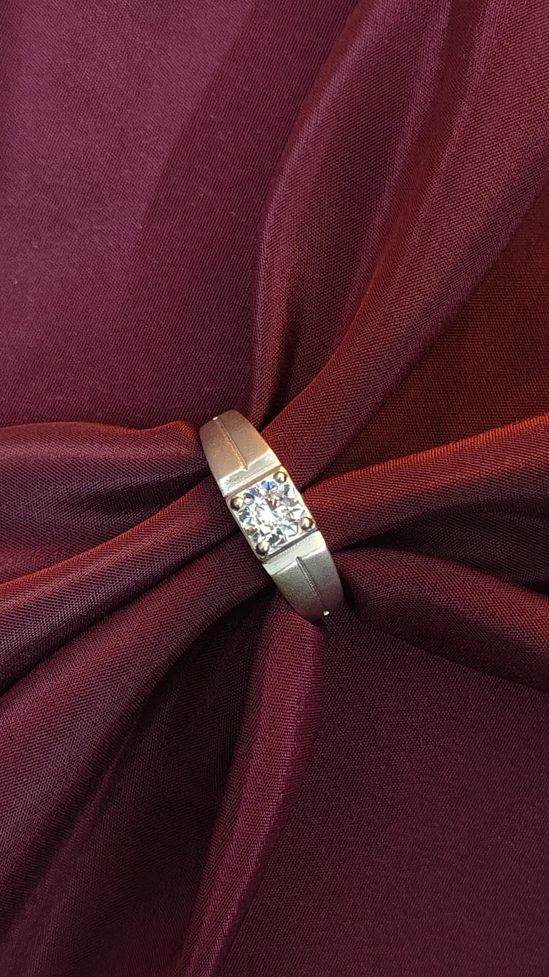 Gold ring with a diamond on a burgundy fabric background