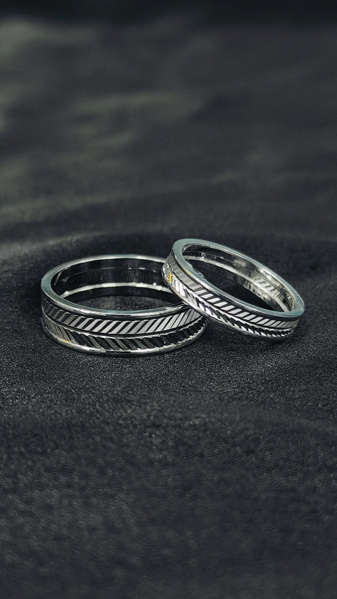 Two silver rings with textured design on a dark fabric background