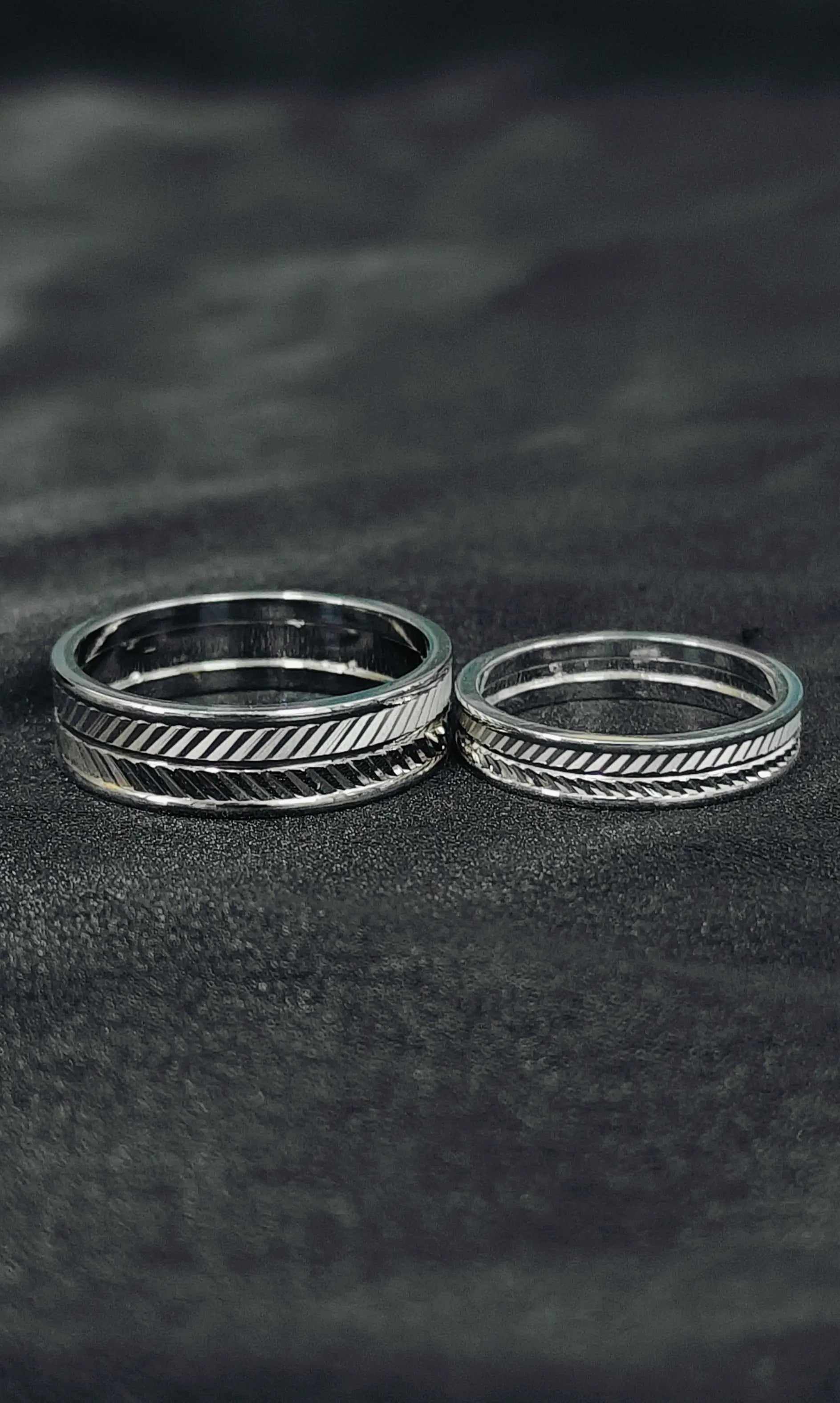 Two silver rings with textured designs on a dark textured surface