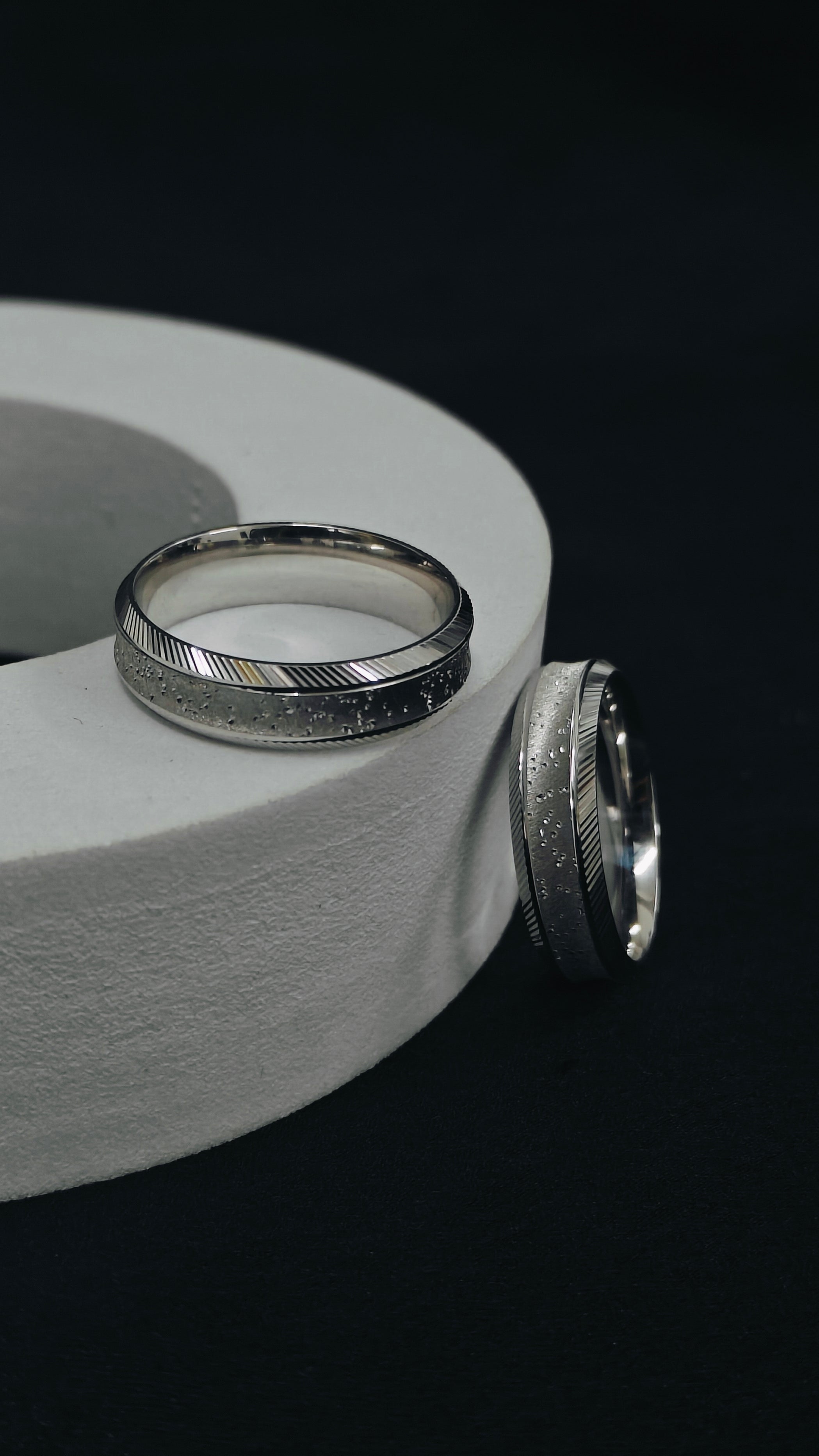 Two silver rings on a gray cylindrical object with a black background