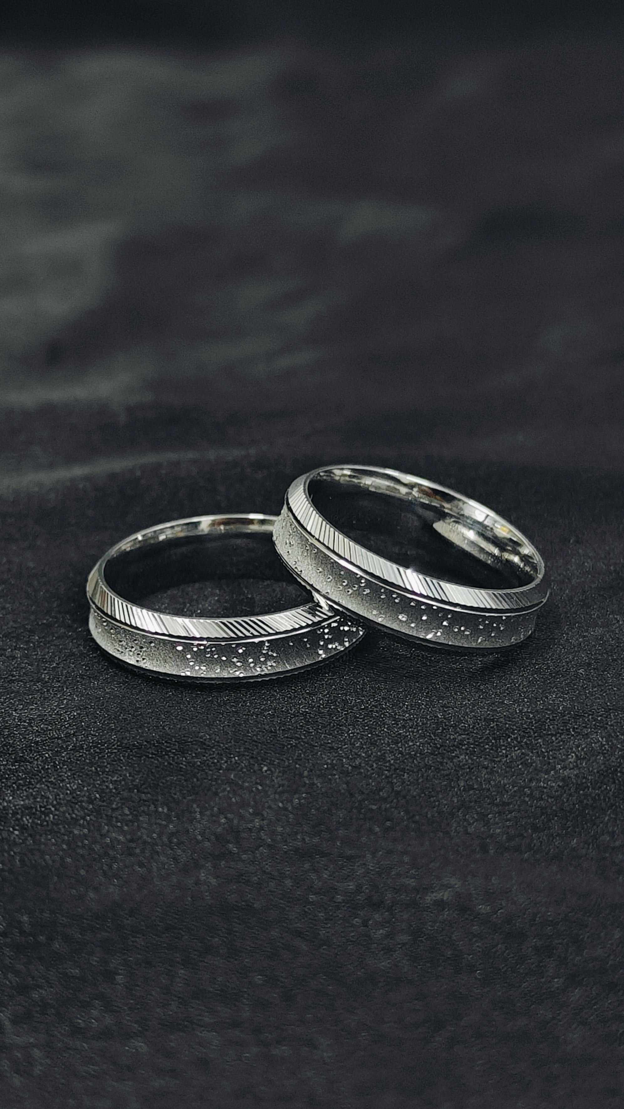 Two silver rings on a dark textured surface