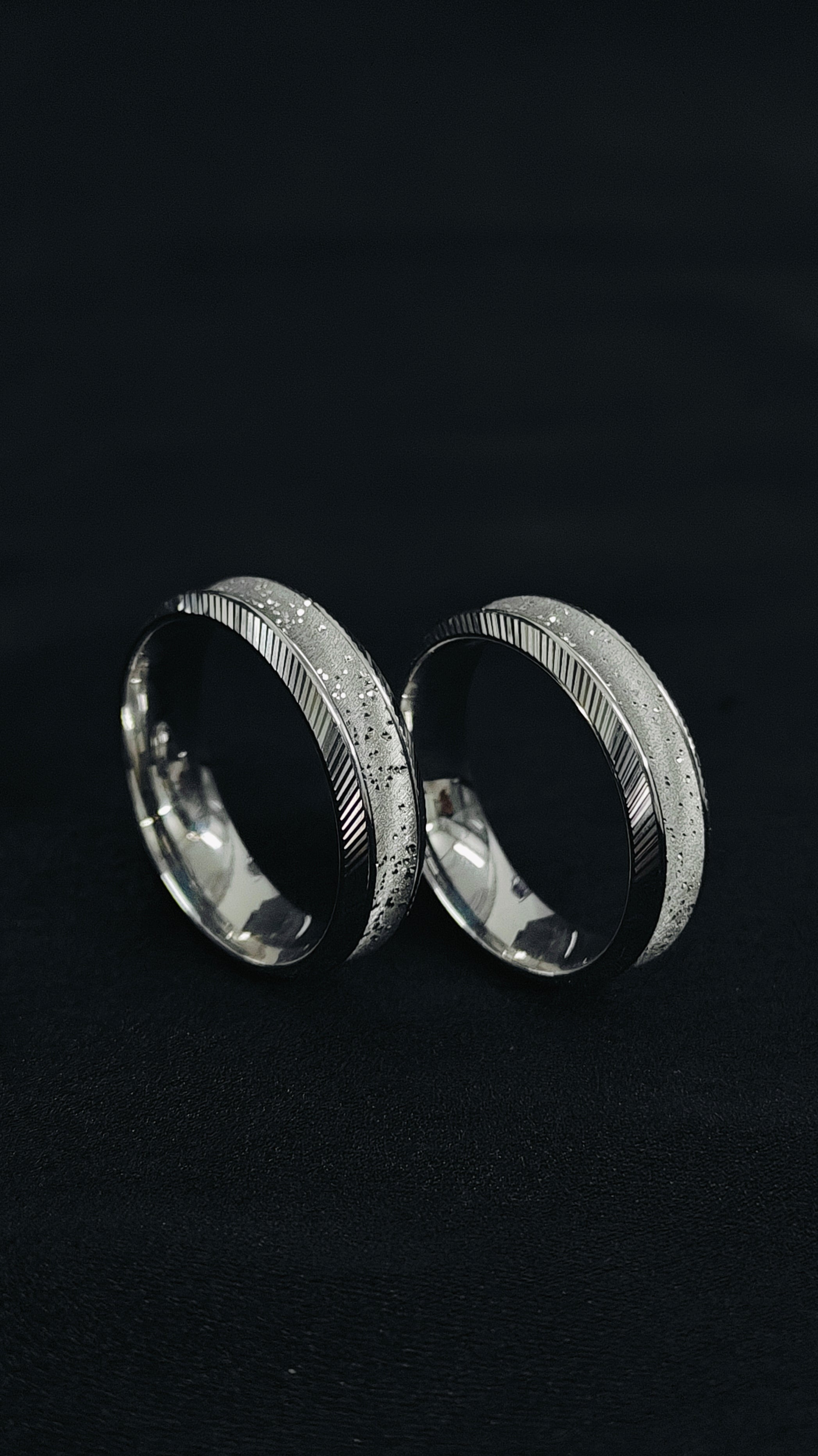 Two silver rings with textured band design on a black background