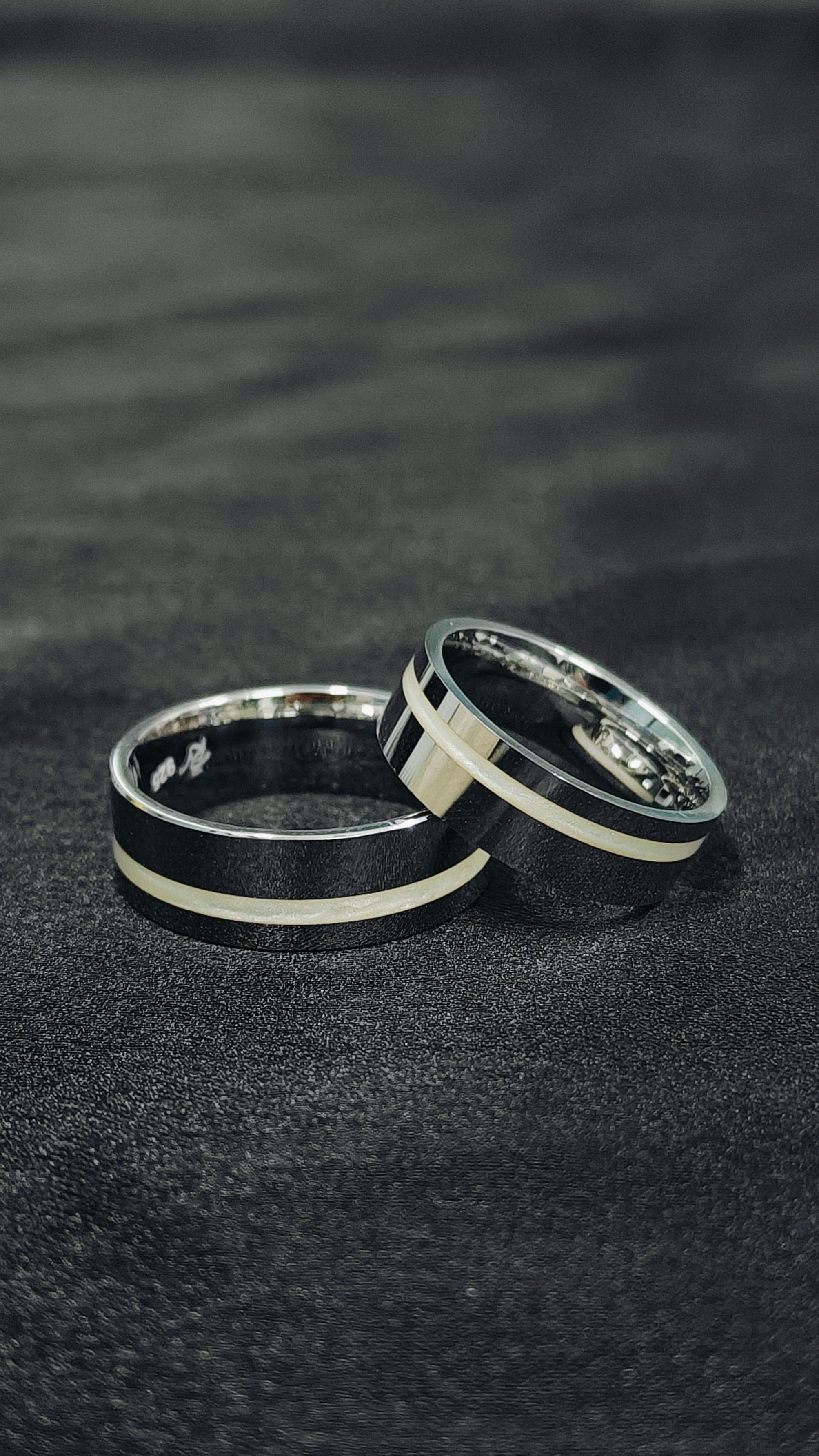 Two black and silver rings on a dark textured surface
