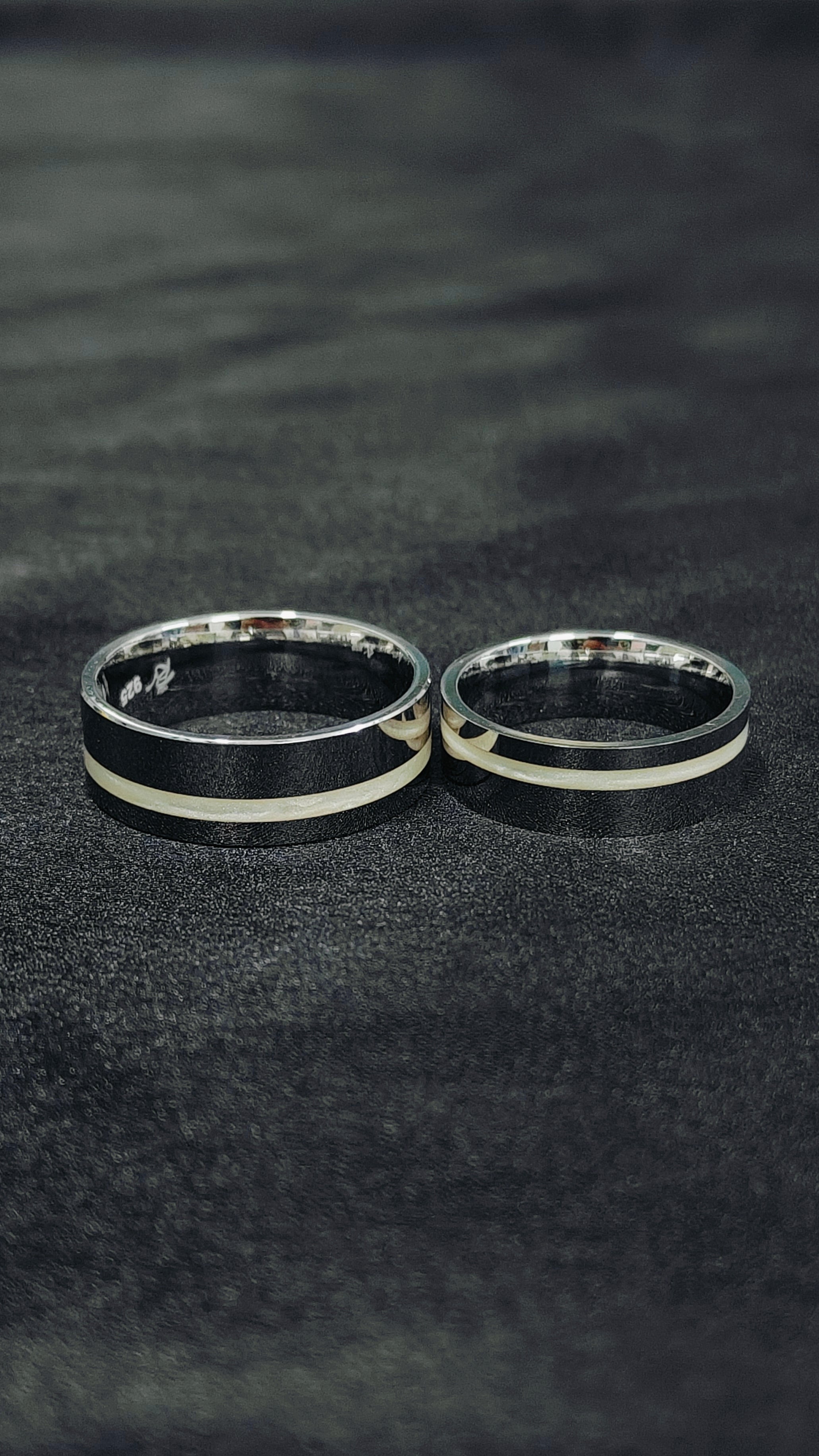 Two silver rings with black accents on a dark textured surface