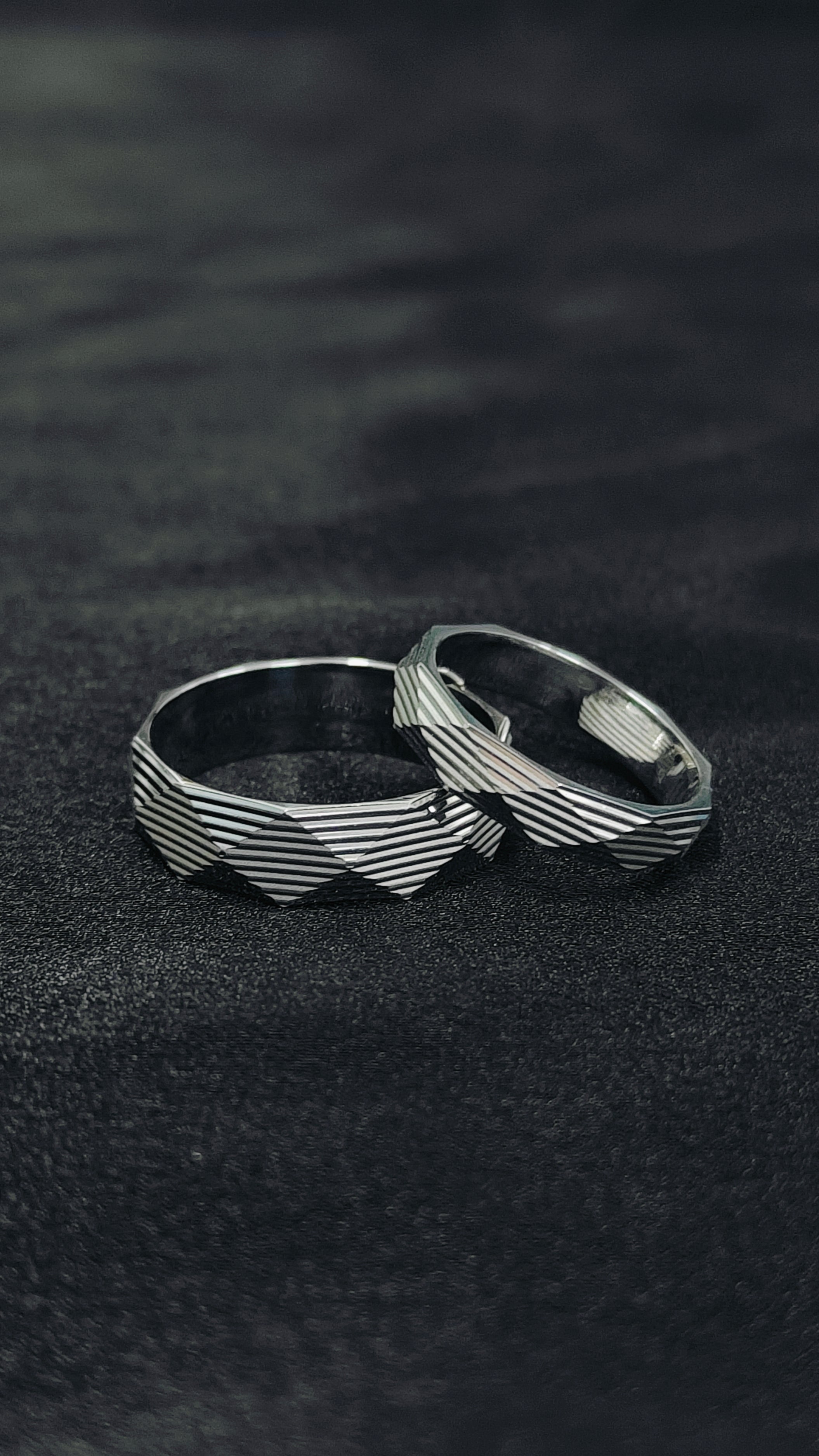 Two silver rings with a wavy design on a black textured surface
