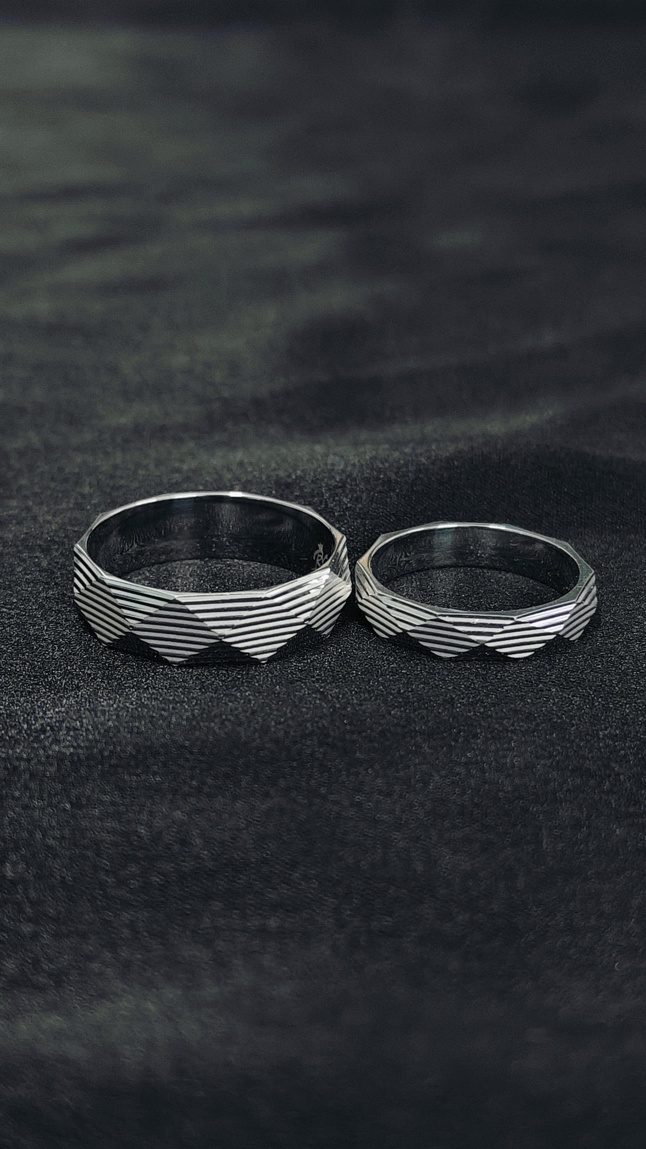 Two silver rings with wavy band design on a dark textured surface