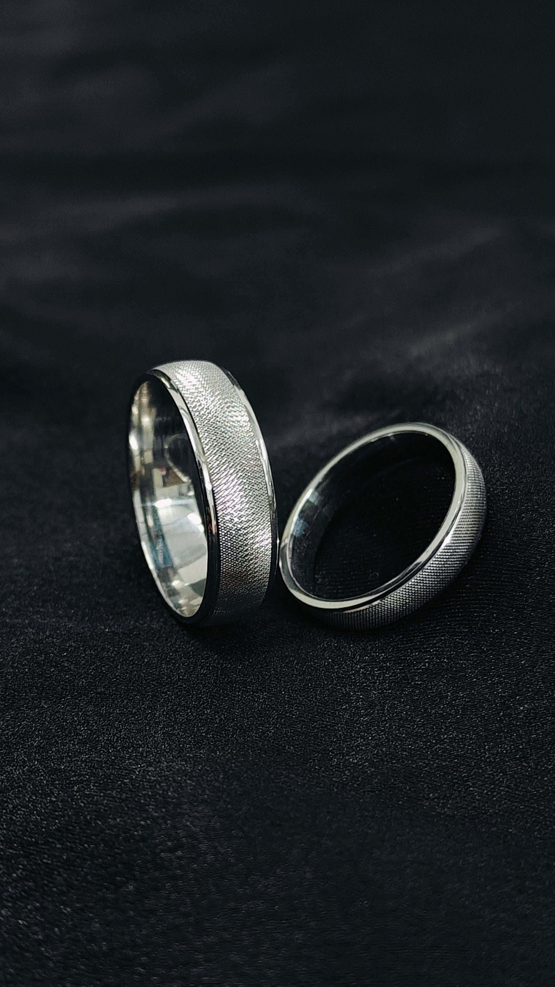 Two silver rings on a dark textured surface
