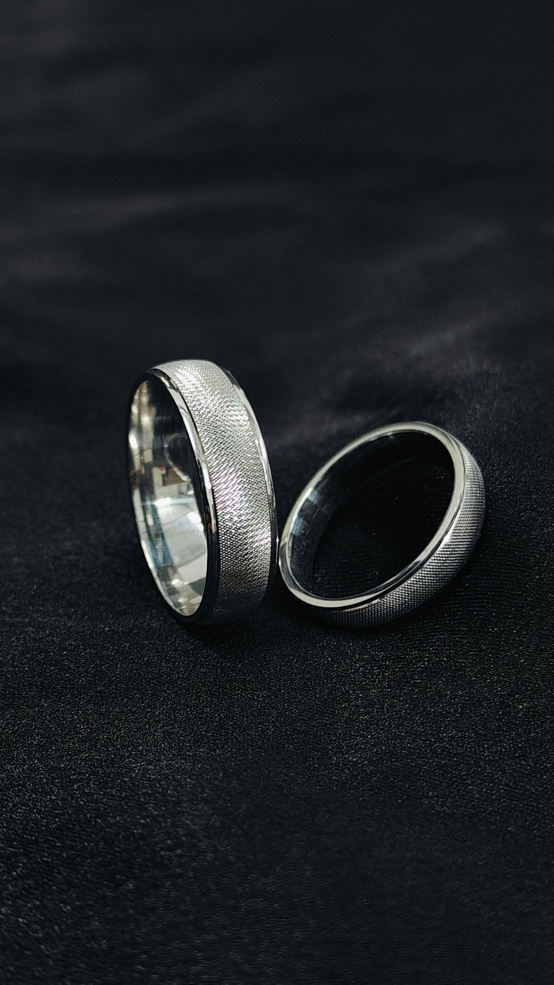 Two silver rings on a dark textured surface