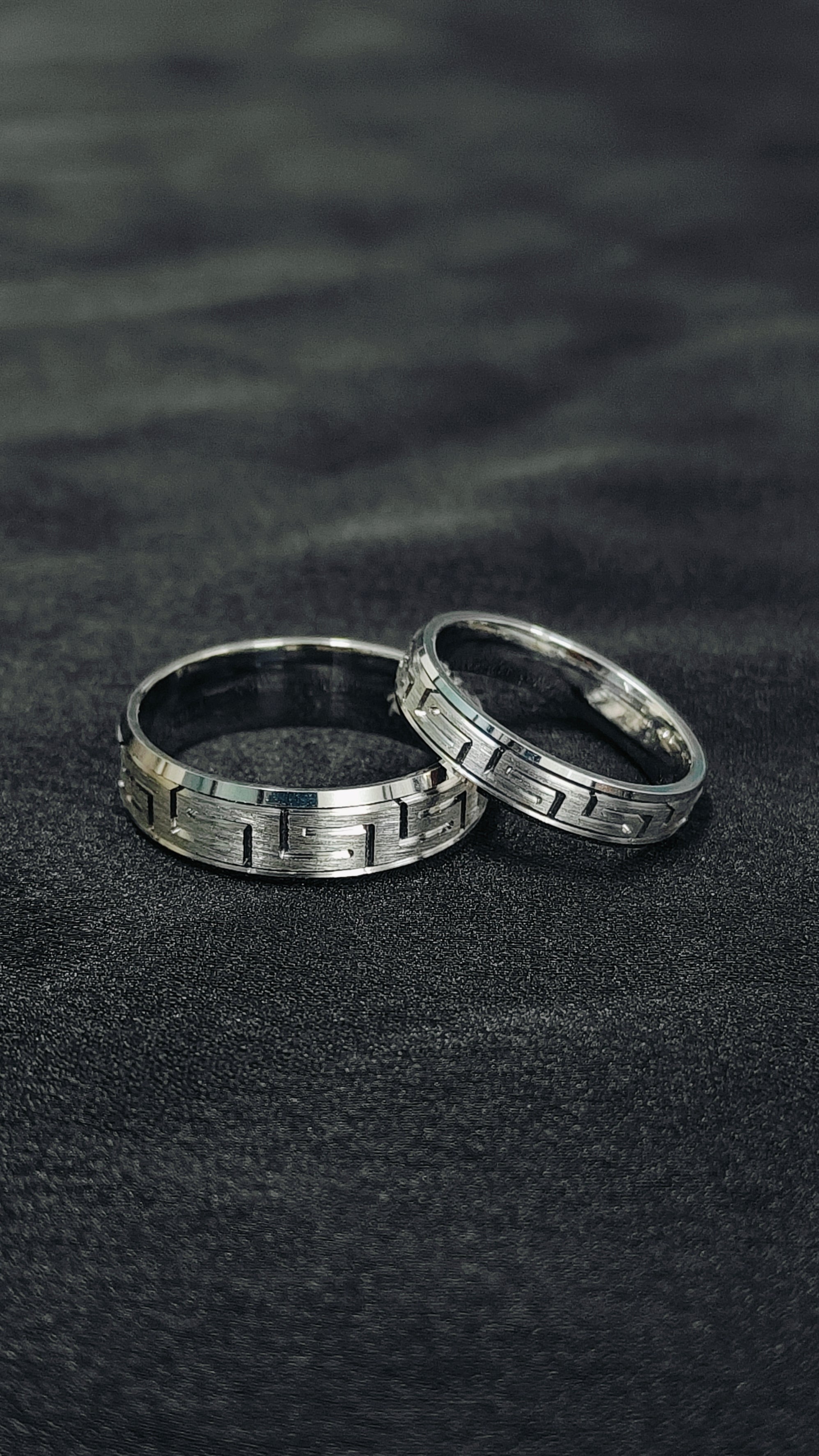 Two silver rings on a dark textured surface