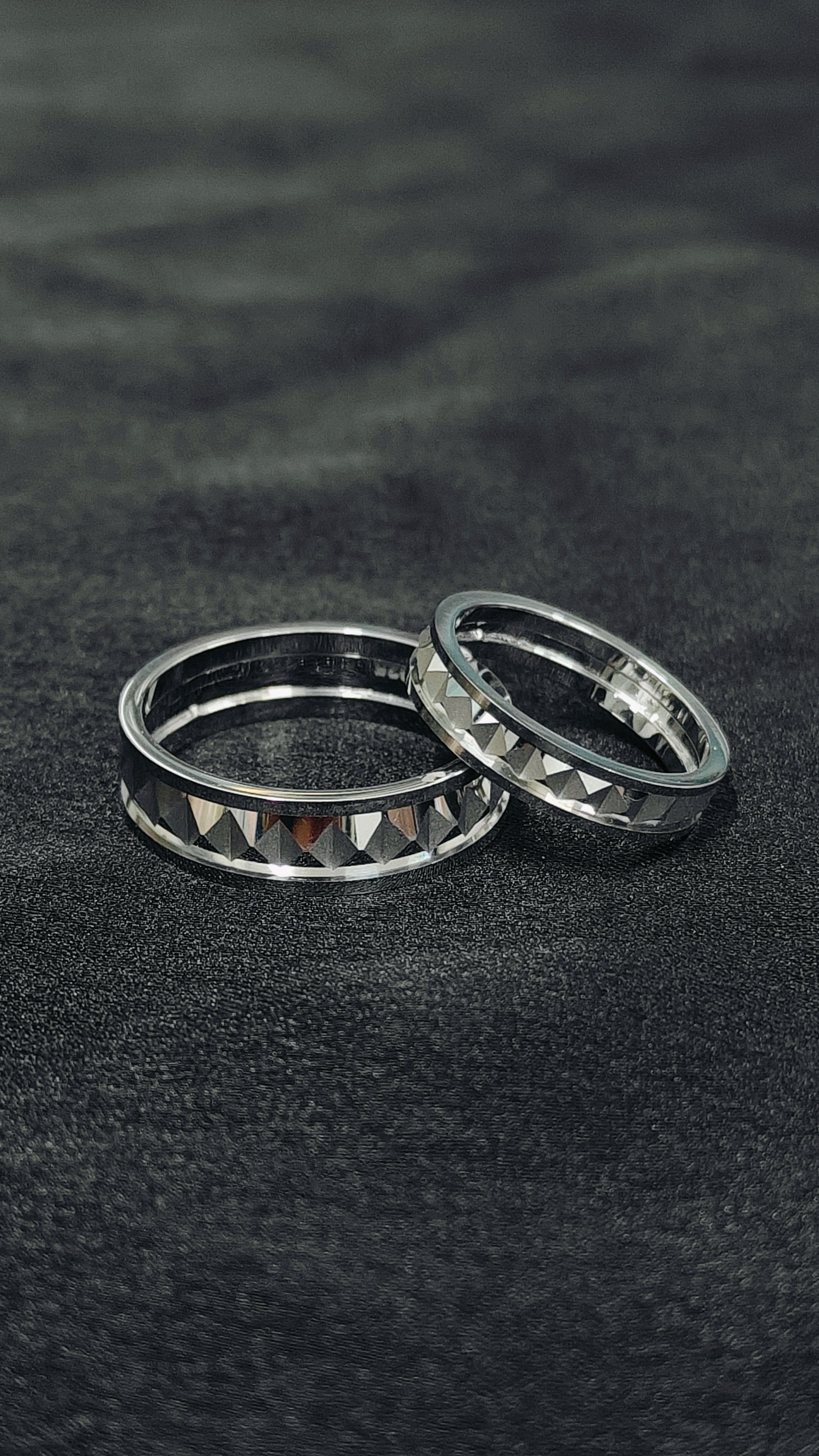 Two silver rings with pyramid designs on a black textured surface