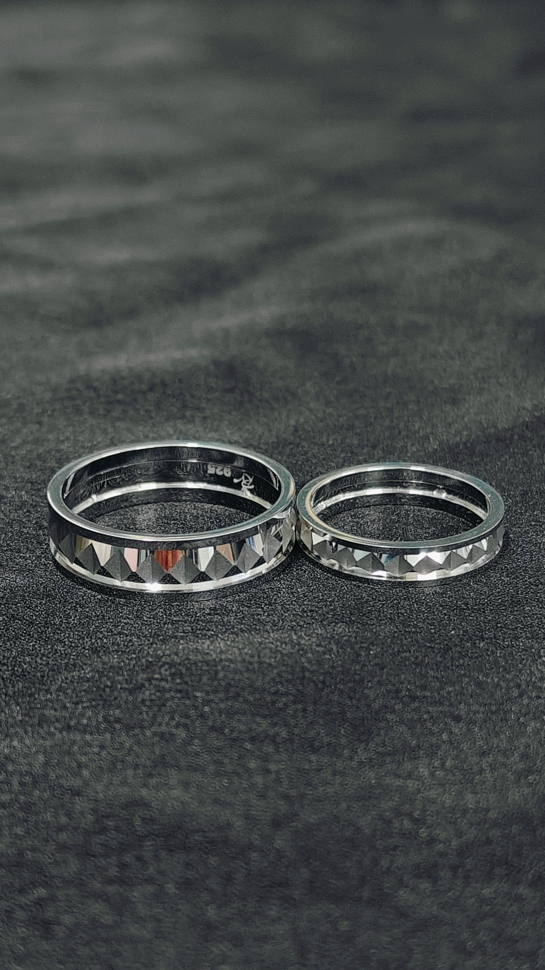 Two silver rings with textured band design on a dark textured surface