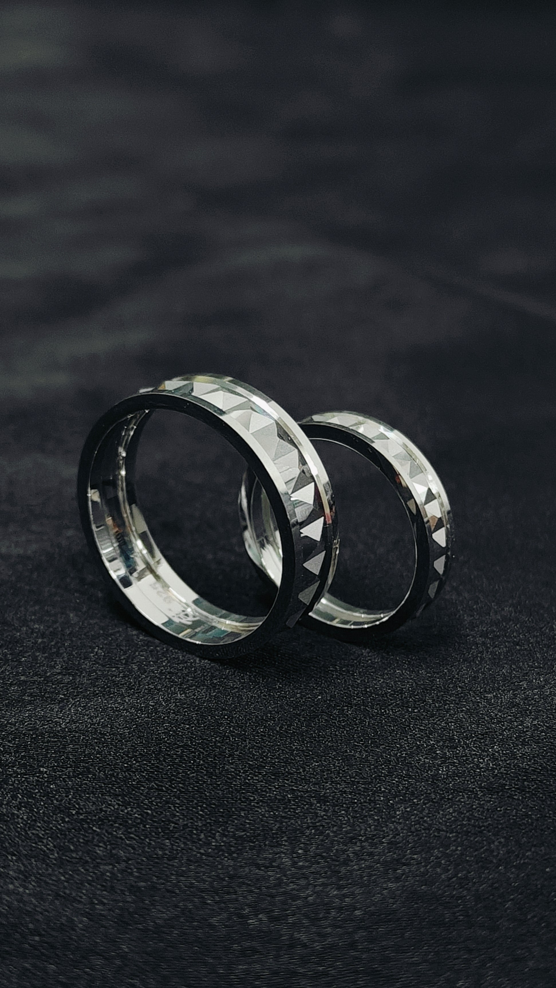 Two silver rings with a textured surface on a dark fabric background