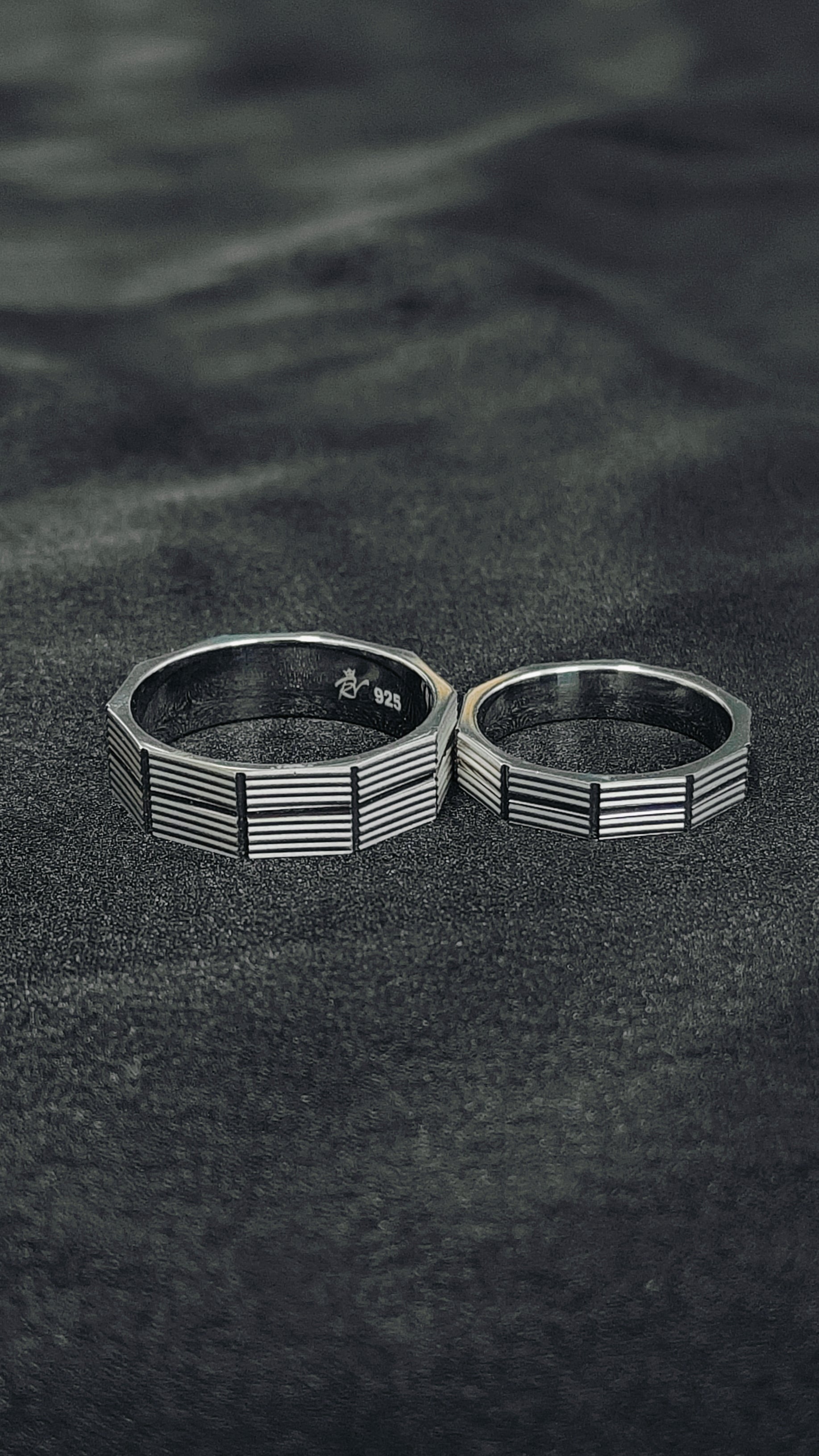 Two silver rings with a geometric design on a dark textured surface