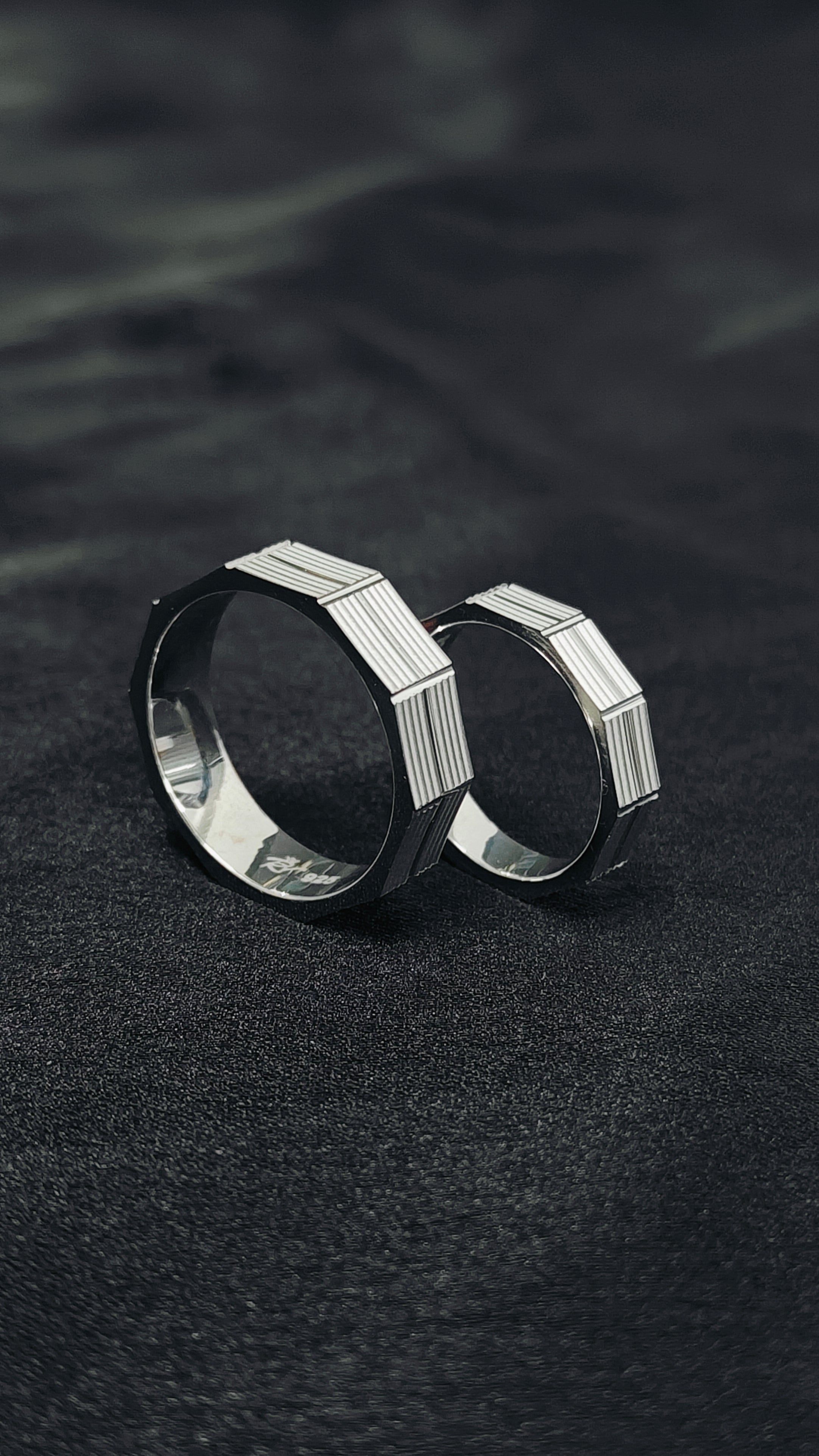 Two silver rings with geometric design on a dark textured surface