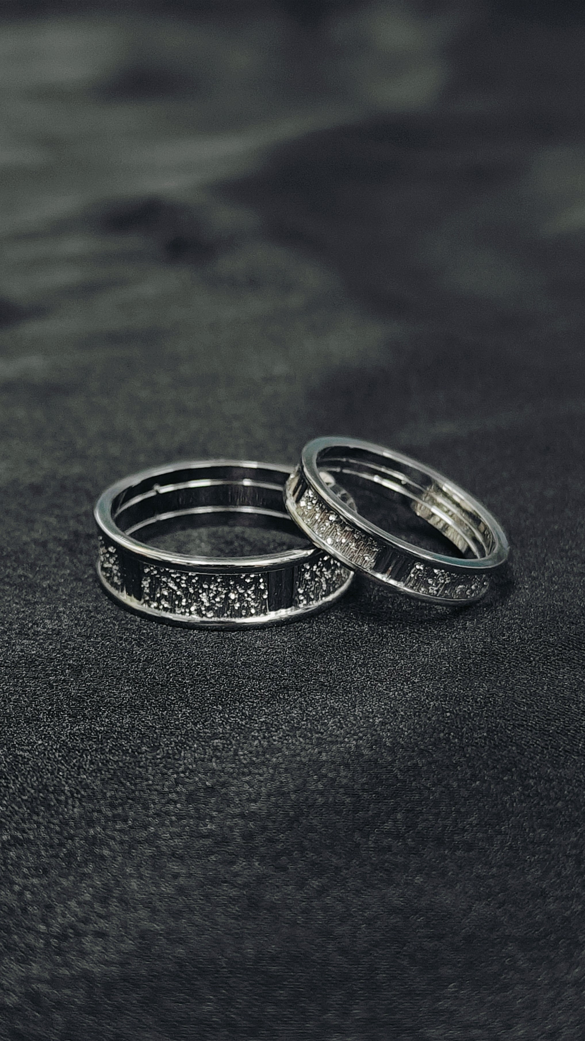 Two silver rings on a dark textured surface