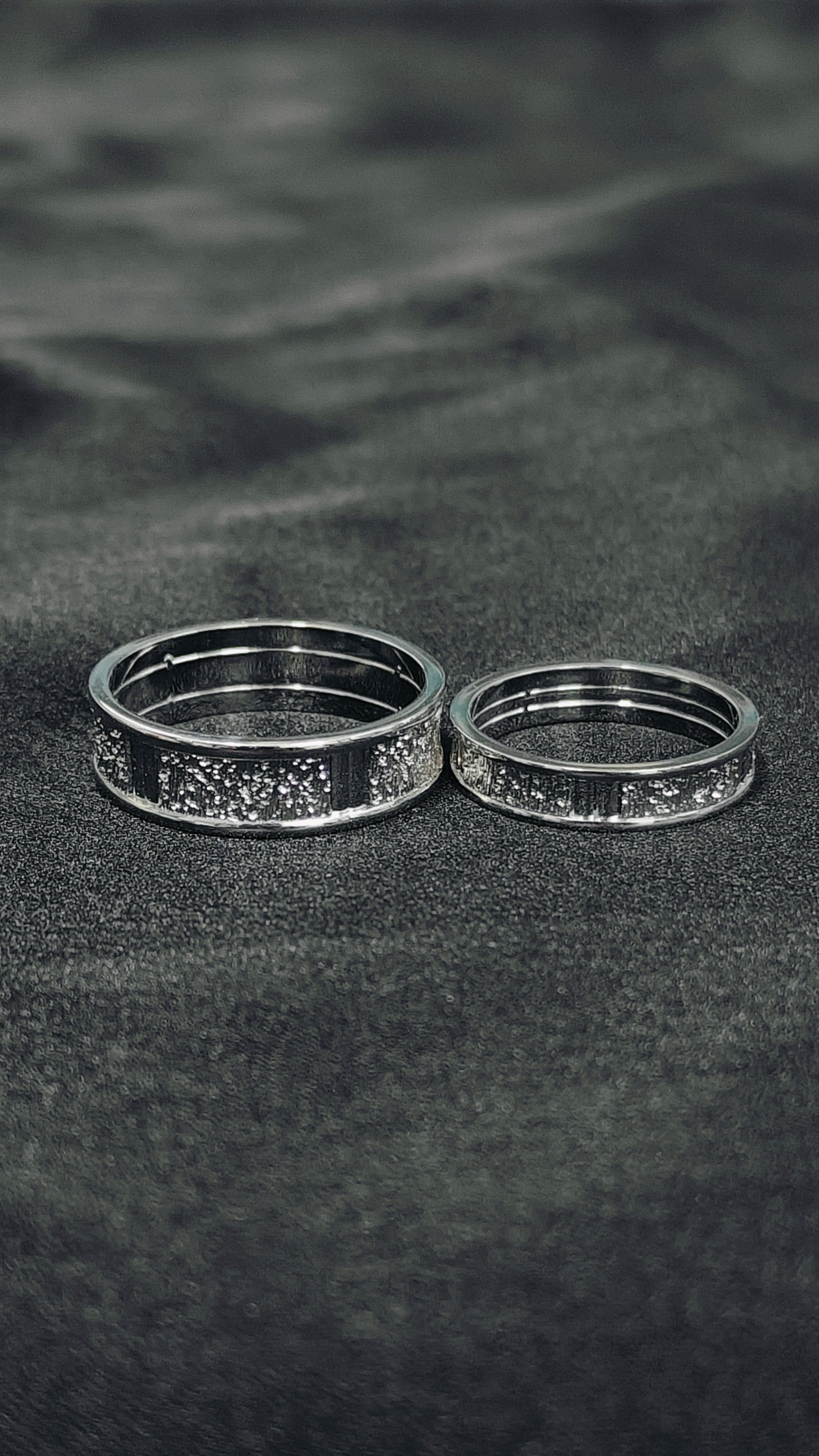 Two silver rings with engraved patterns on a dark textured surface