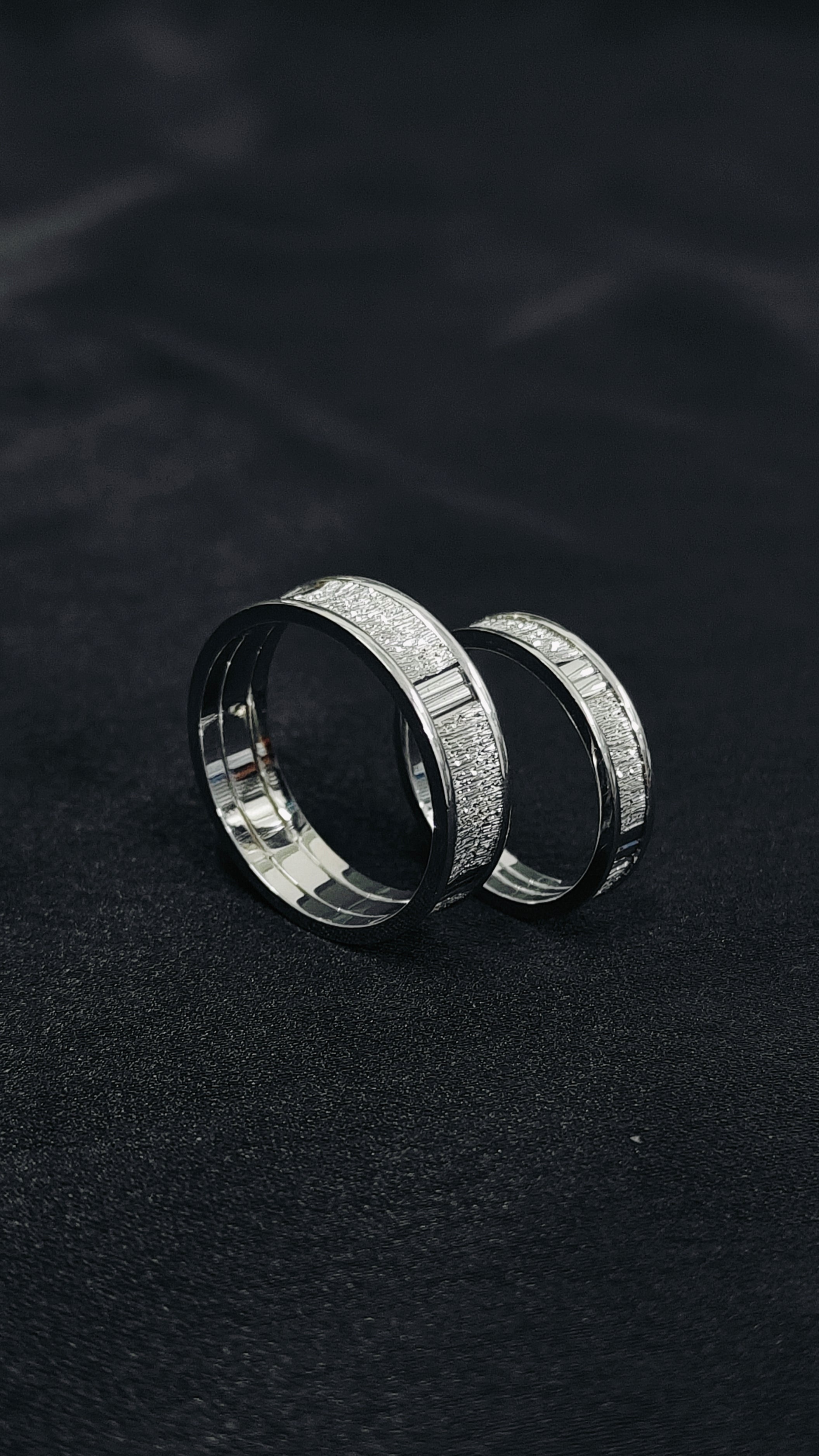 Two silver rings with engraved patterns on a dark textured background