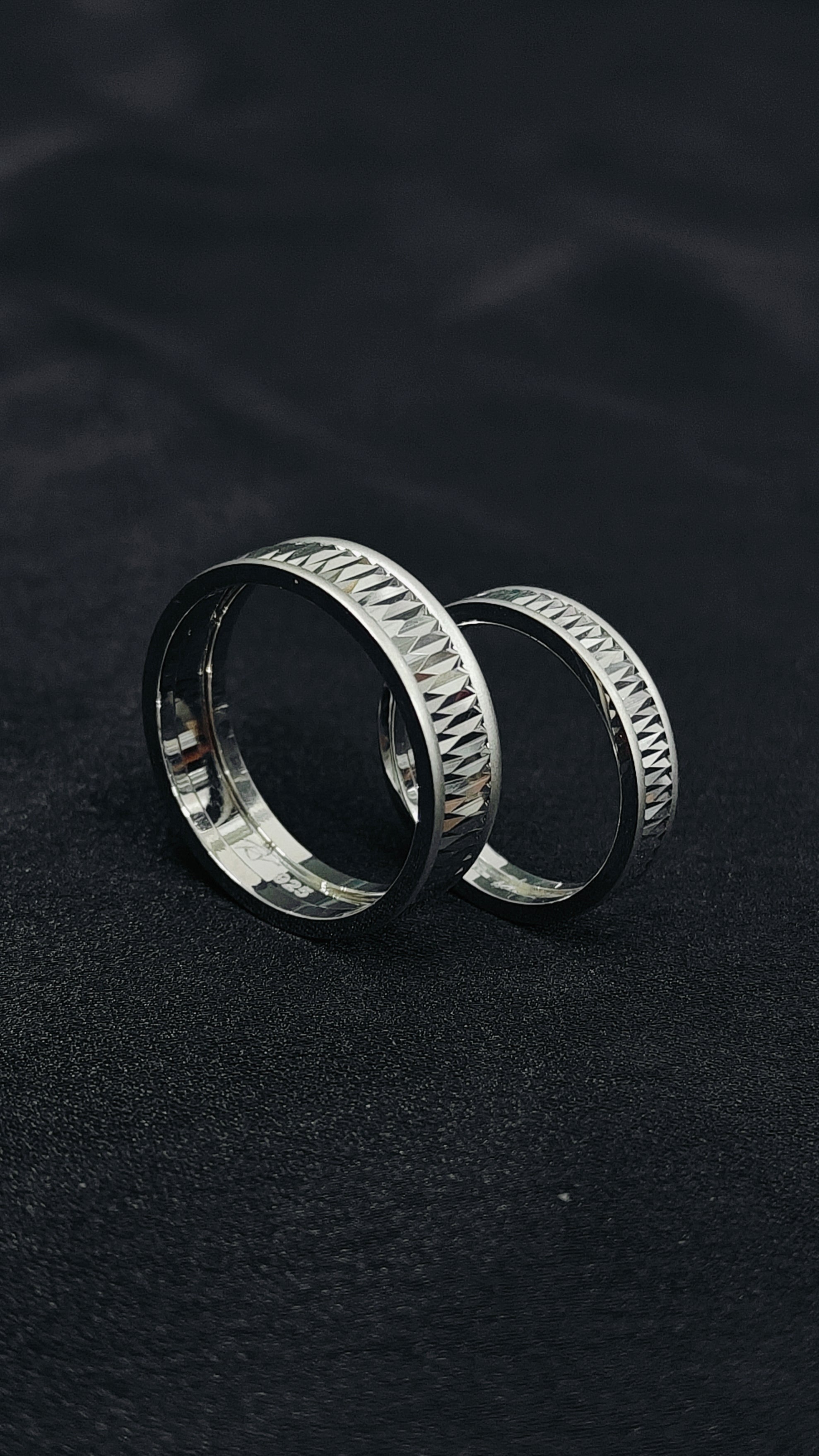 Two silver rings with textured band design on a dark background