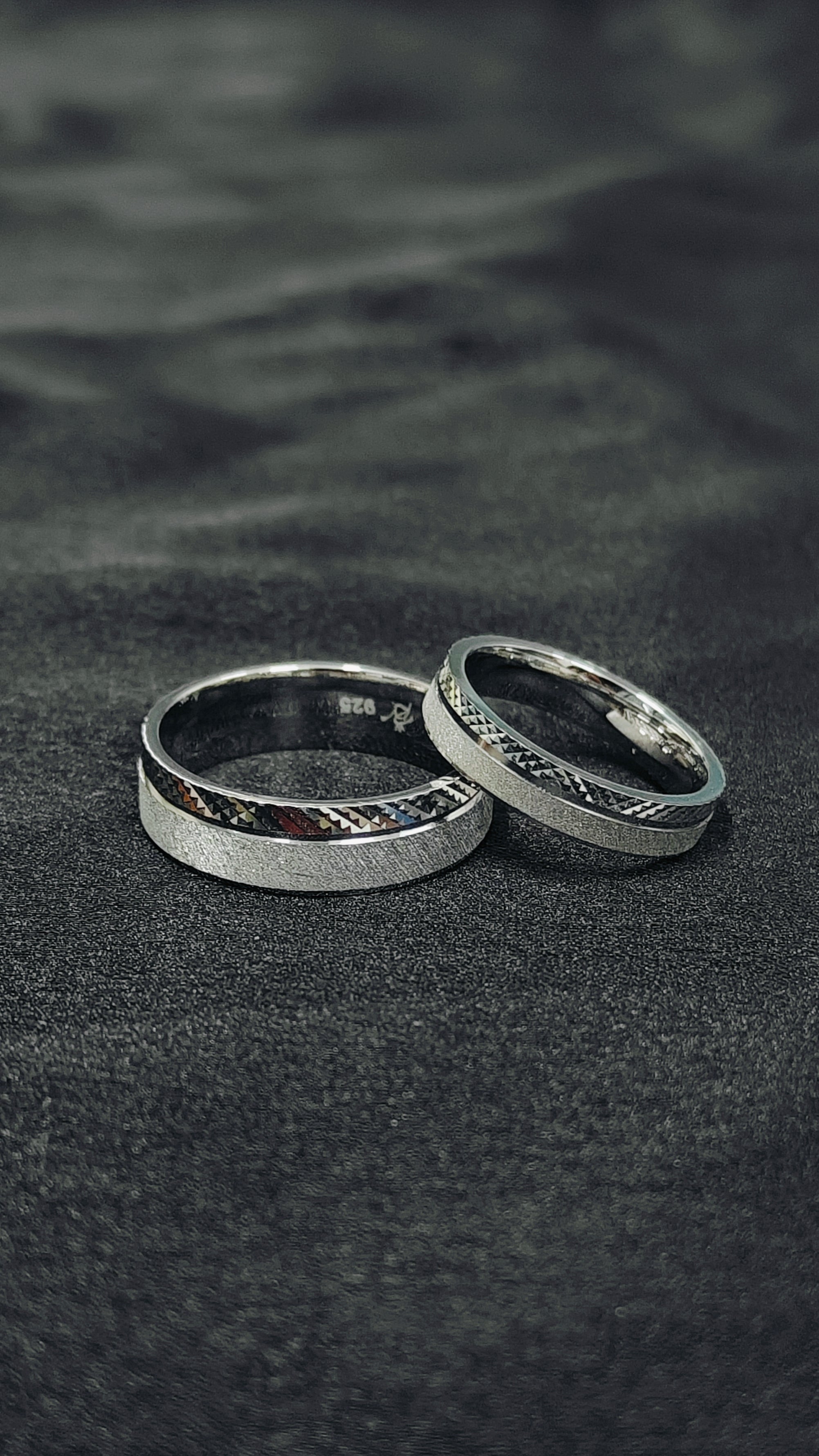 Two silver rings on a dark textured surface