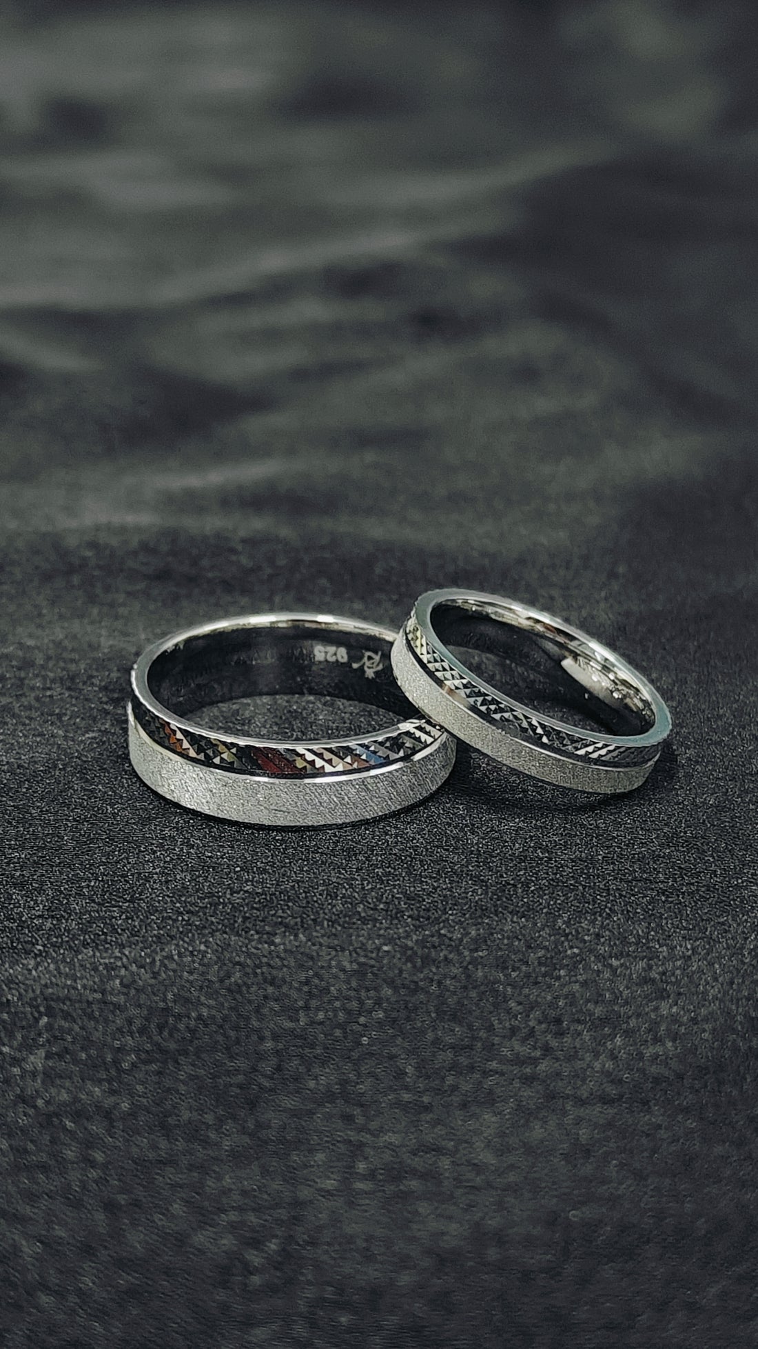 Two silver rings on a dark textured surface